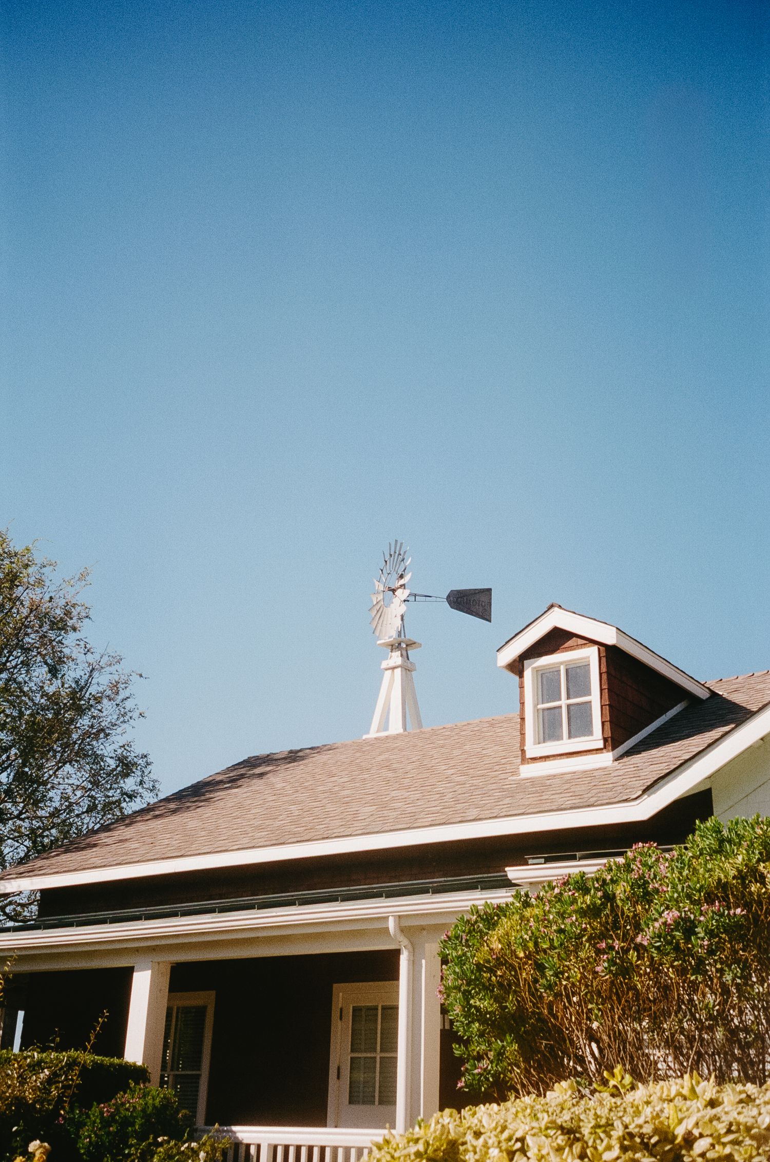Single story ranch house with brown roof and white trim against bright blue sky.