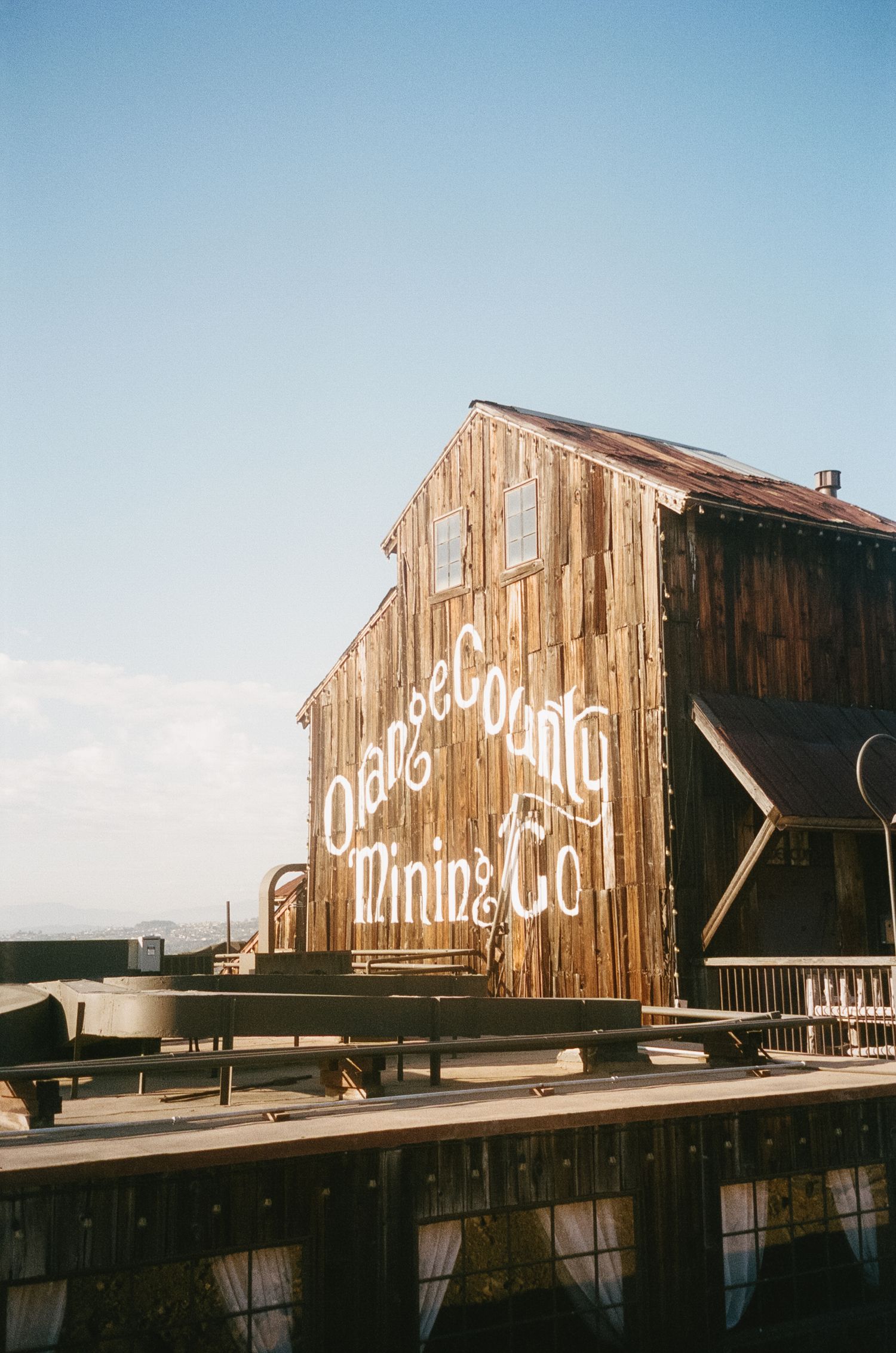 Three vintage wooden buildings with faded white lettering on their weathered sides stand against a blue sky.