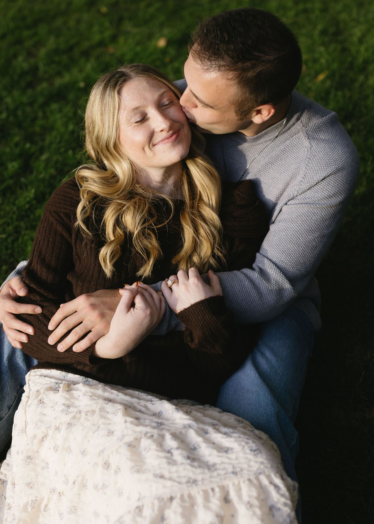 A romantic couple embraces outdoors with soft natural lighting and greenery in the background.