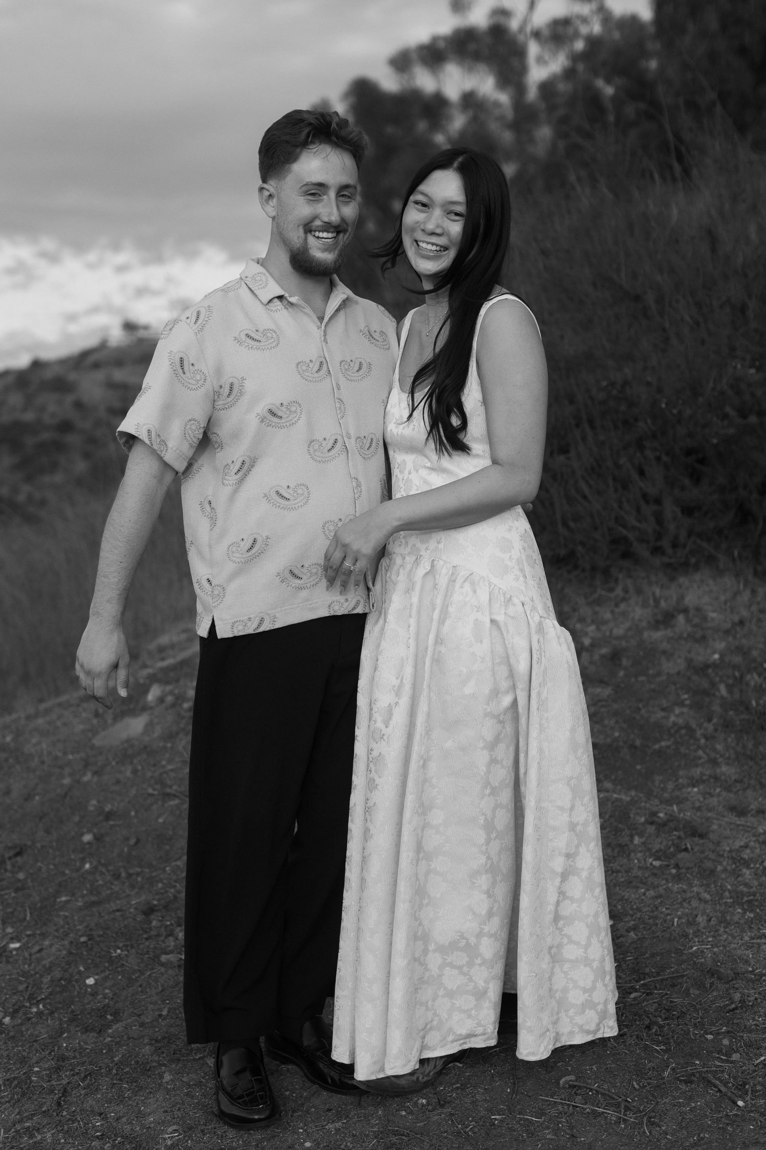 A couple poses together outdoors in black and white, wearing casual attire and sharing intimate moments.
