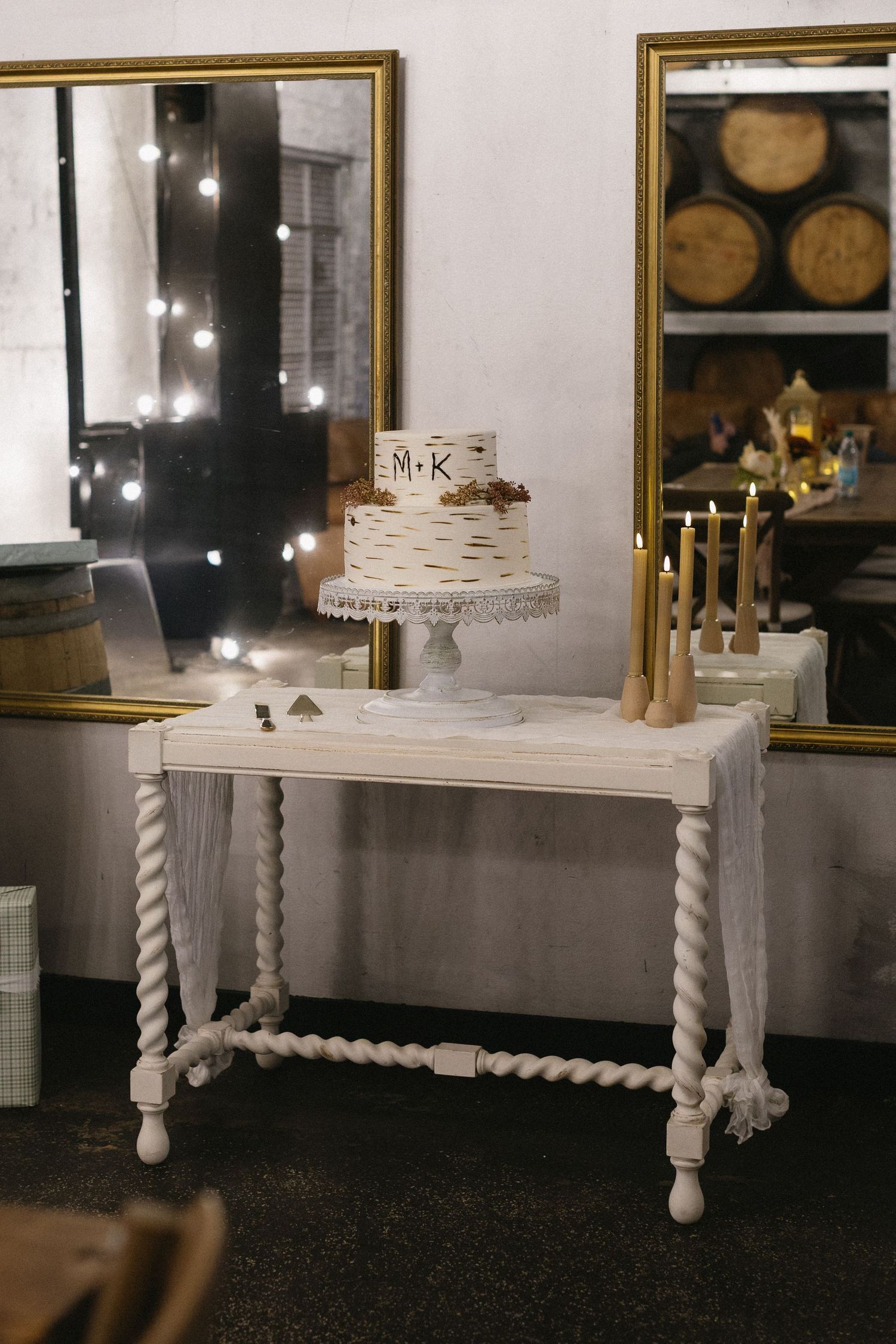 White decorative table with twisted legs displaying candles and decor against a wall with wine barrels.