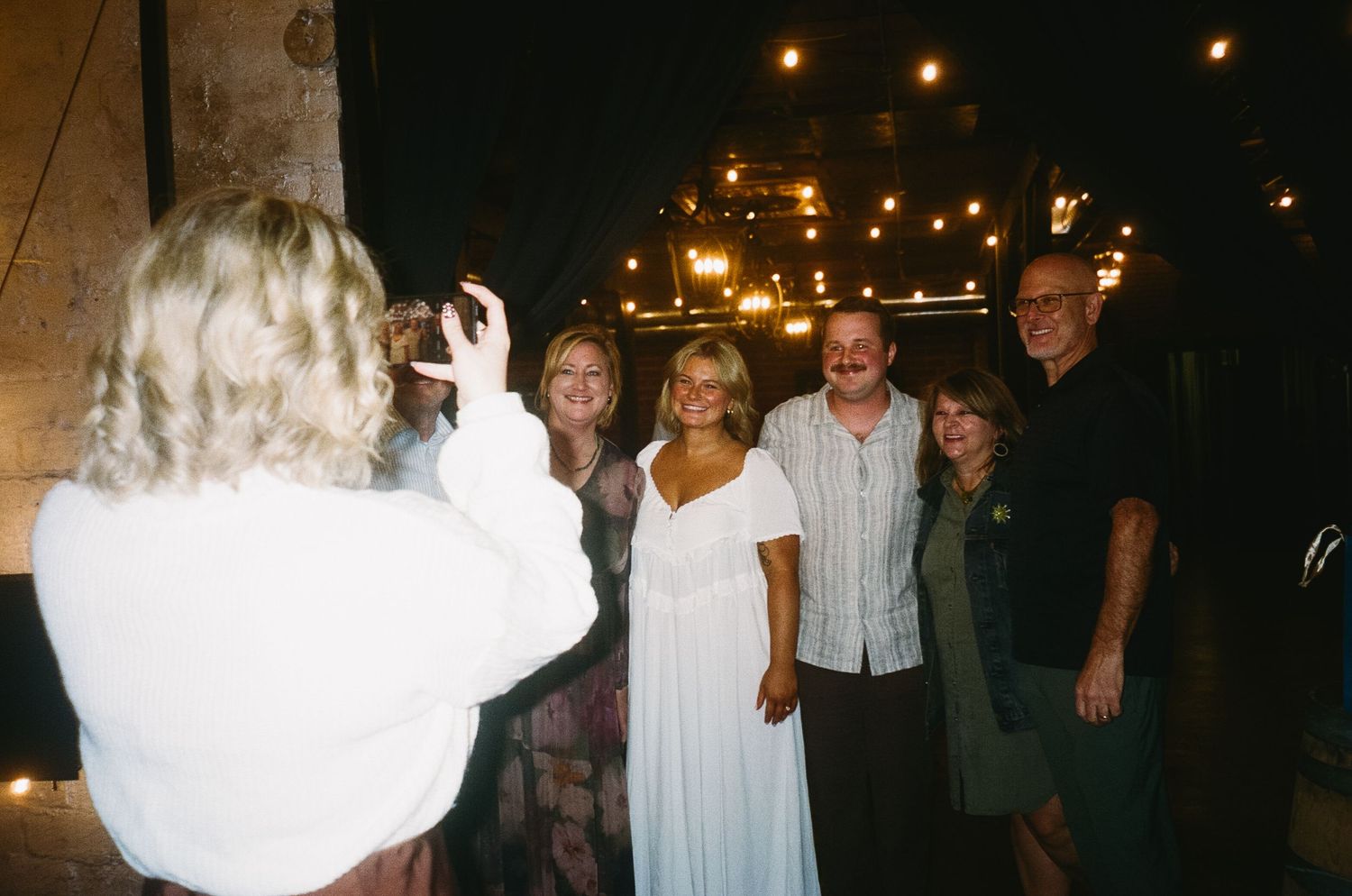 Group photo being taken at nighttime event with string lights in background.