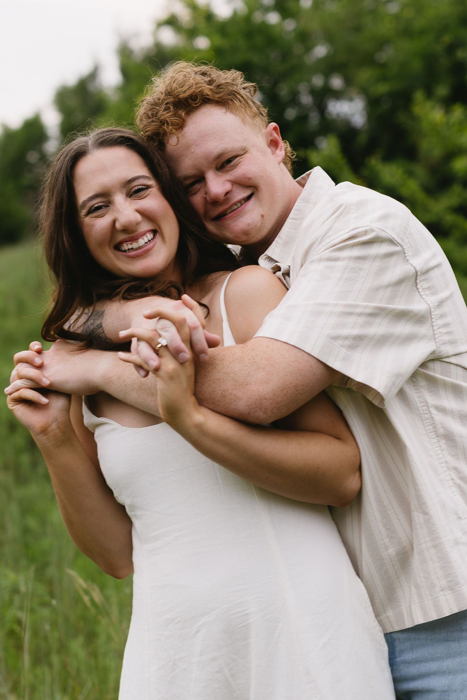 A playful couple in white outfits shares joyful embraces in a sunny meadow setting.