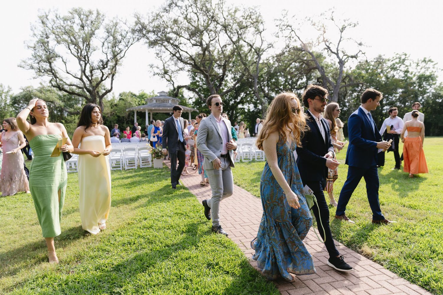 Wedding guests dance and celebrate on a lush green lawn during an outdoor reception party.