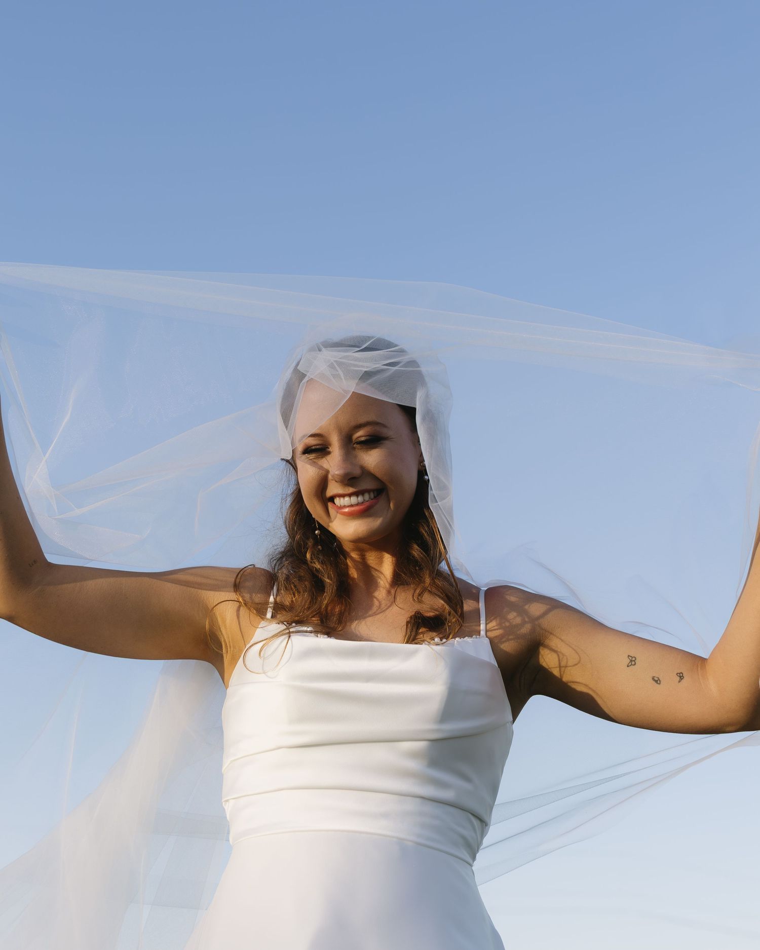 A bridal portrait series against a bright blue sky with a flowing white veil catching sunlight.