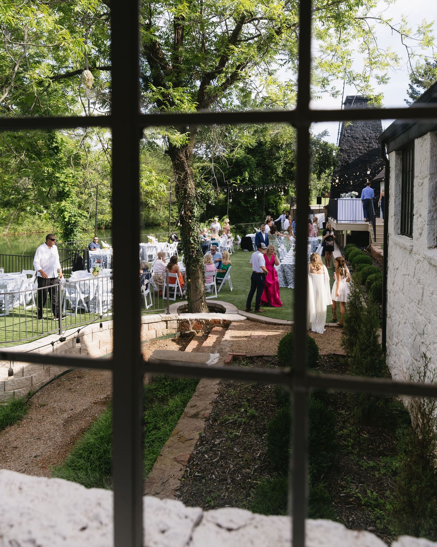 View through window frames of an outdoor wedding reception area with guests mingling.