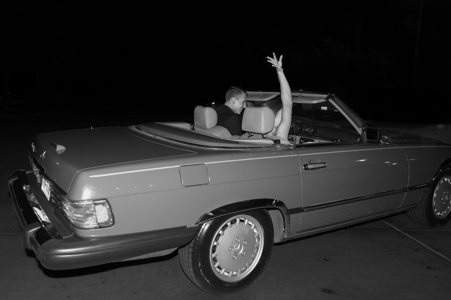 A vintage convertible car with someone's arm raised in celebration at night.