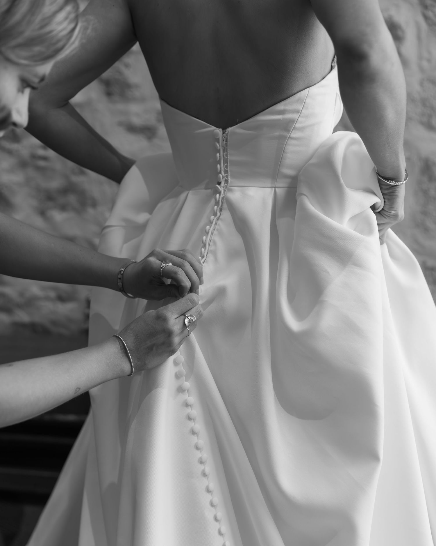 Close-up shots of buttons being fastened on the back of an elegant white wedding dress.
