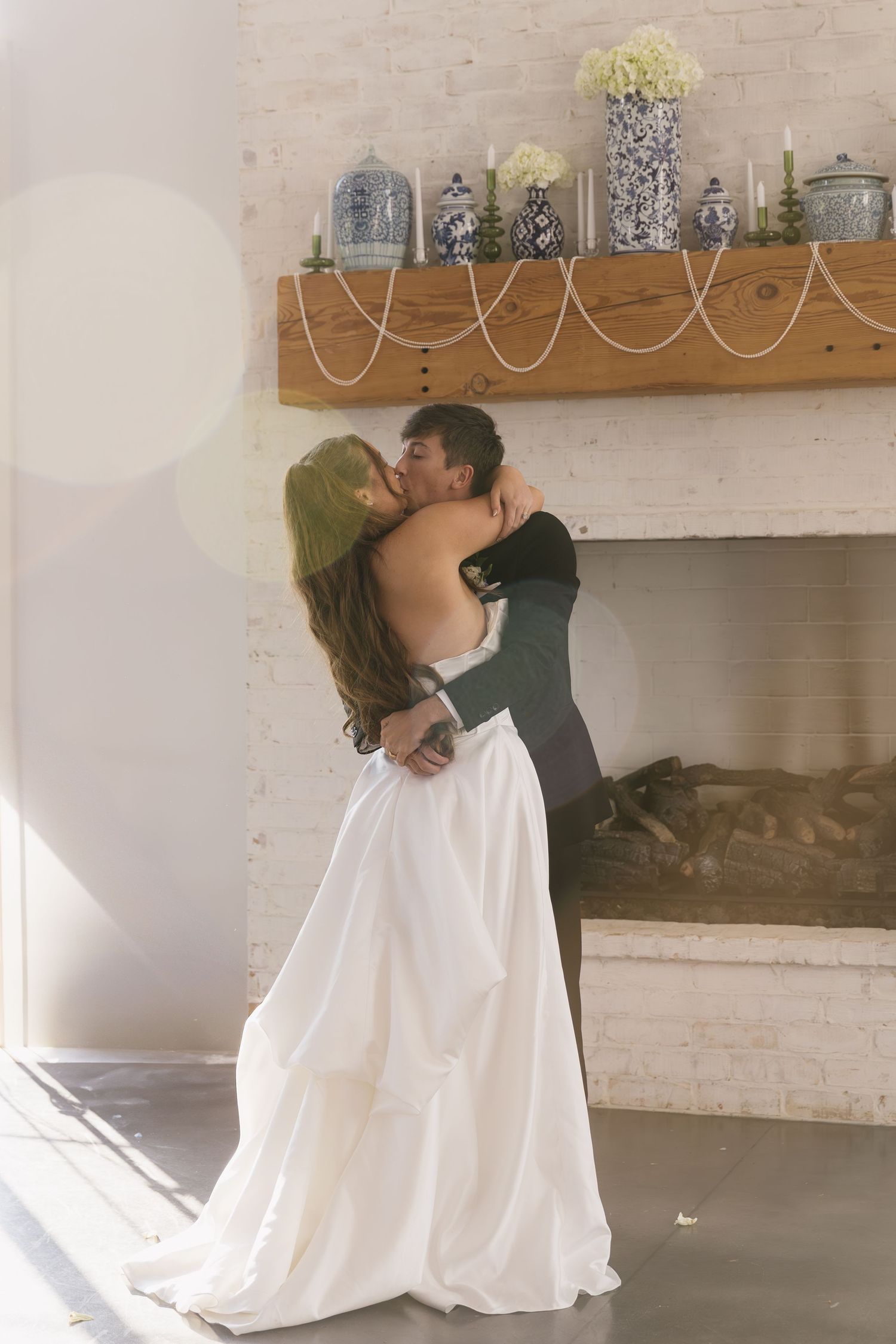 Romantic moment between newlyweds sharing a kiss by a decorated mantle with glass jars.