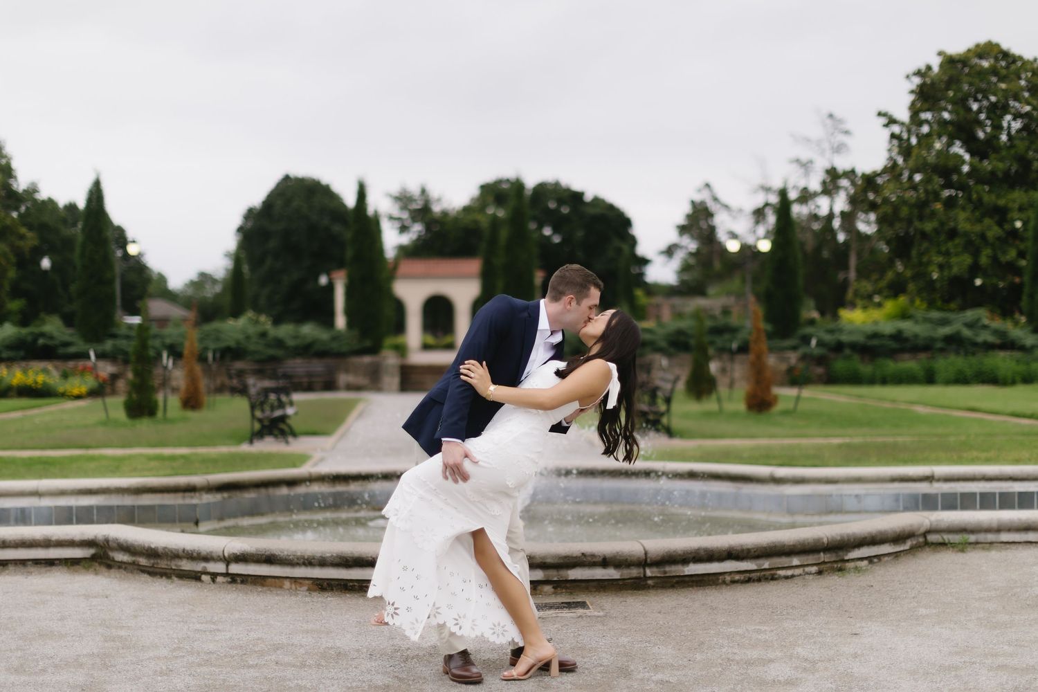 A wedding couple sharing a romantic dip pose outdoors in a lush garden setting.