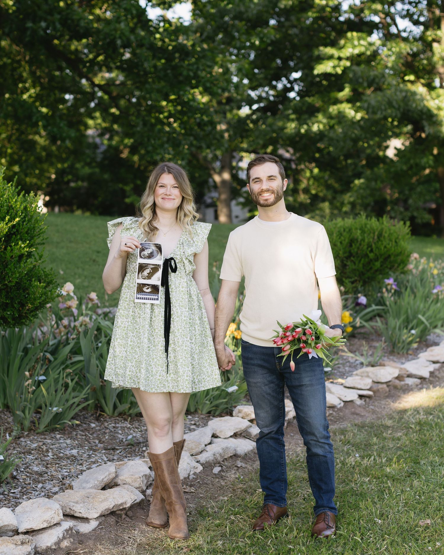 Pregnancy announcement photoshoot in garden setting with couple holding sonogram and flowers.