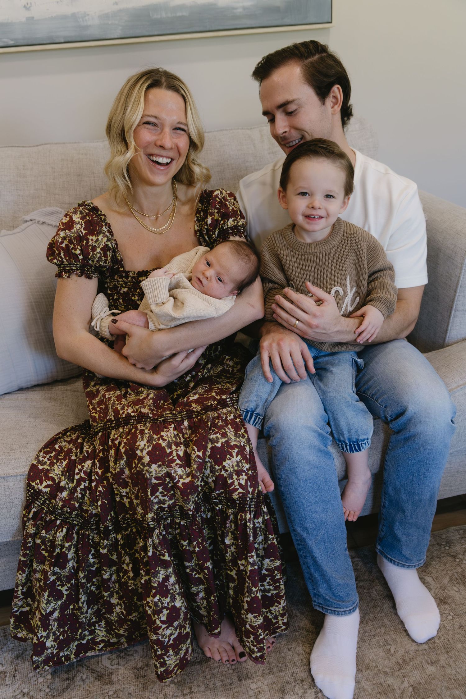 Family relaxing together on grey couch wearing casual clothing.