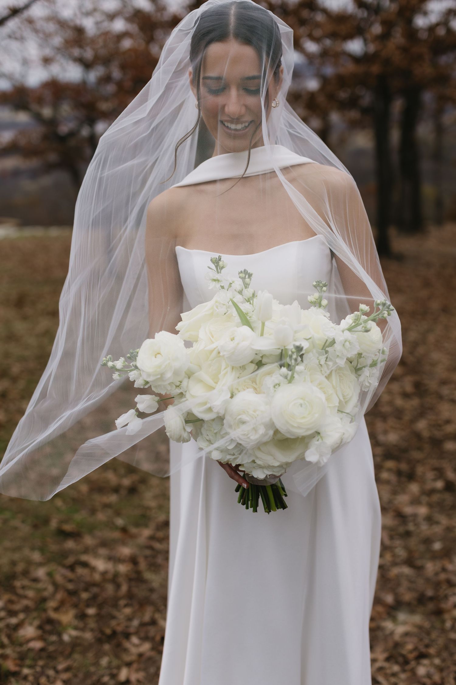 Bride in flowing white dress holding a luxurious bouquet of white roses and greenery.