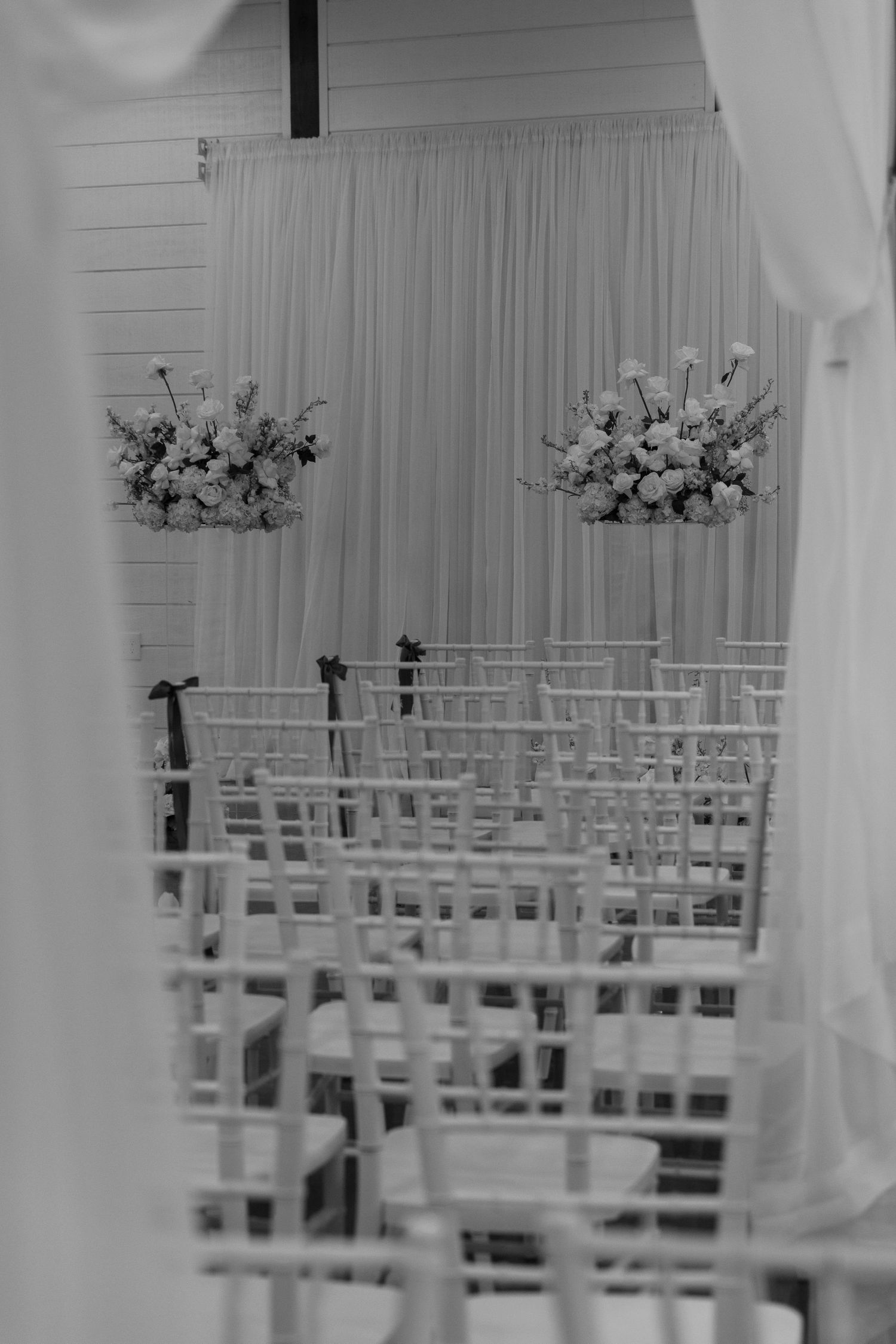 White chairs arranged in rows with floral arrangements at a wedding ceremony venue.