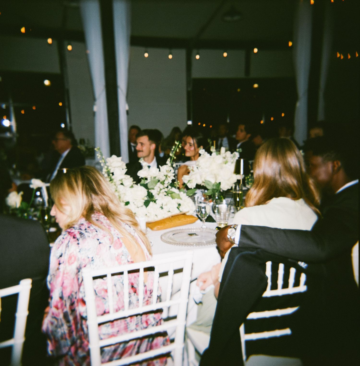 Wedding reception dinner setup with string lights and white chairs.