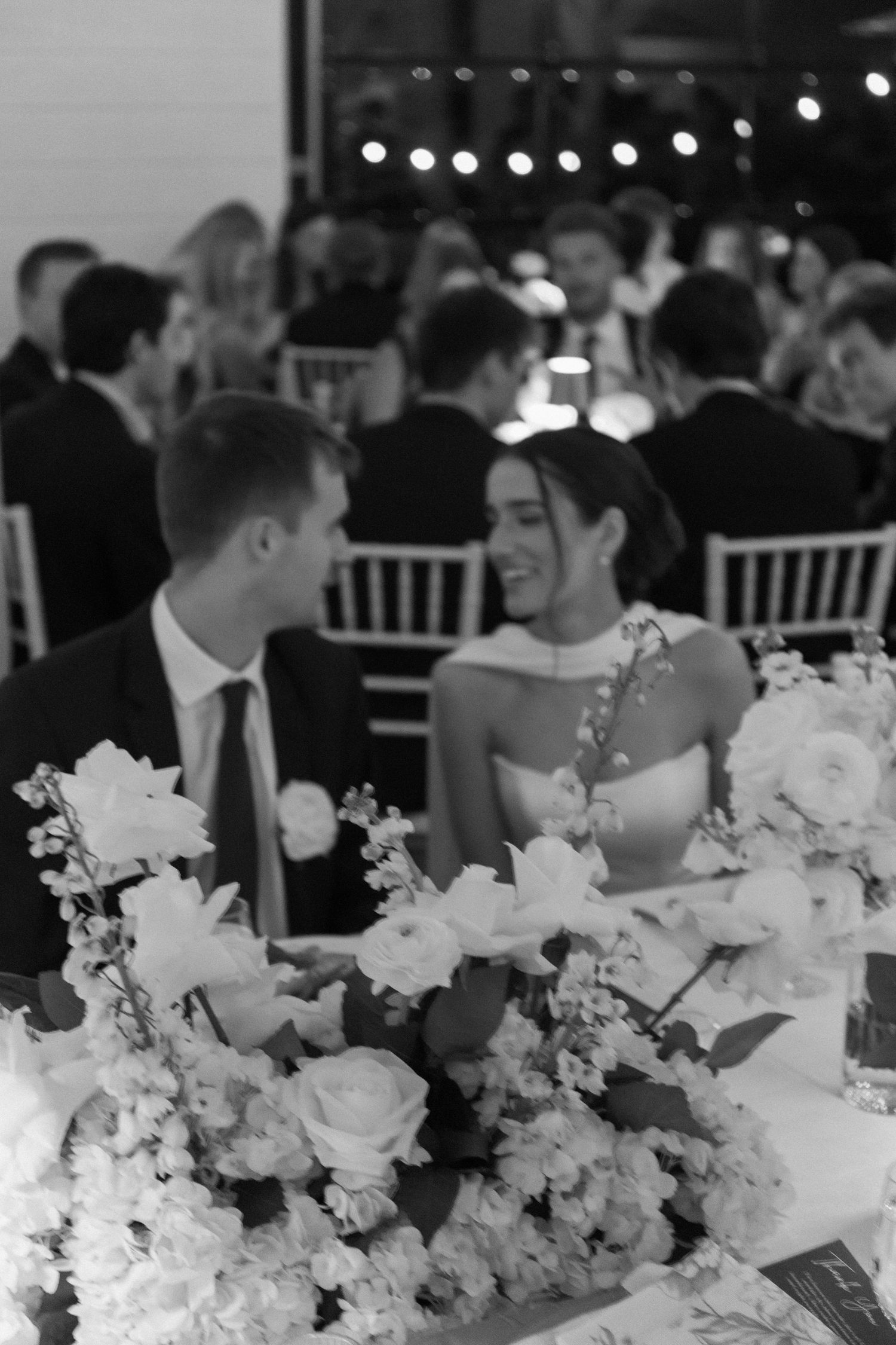 Wedding reception table decorated with elegant white floral centerpieces and string lights overhead.