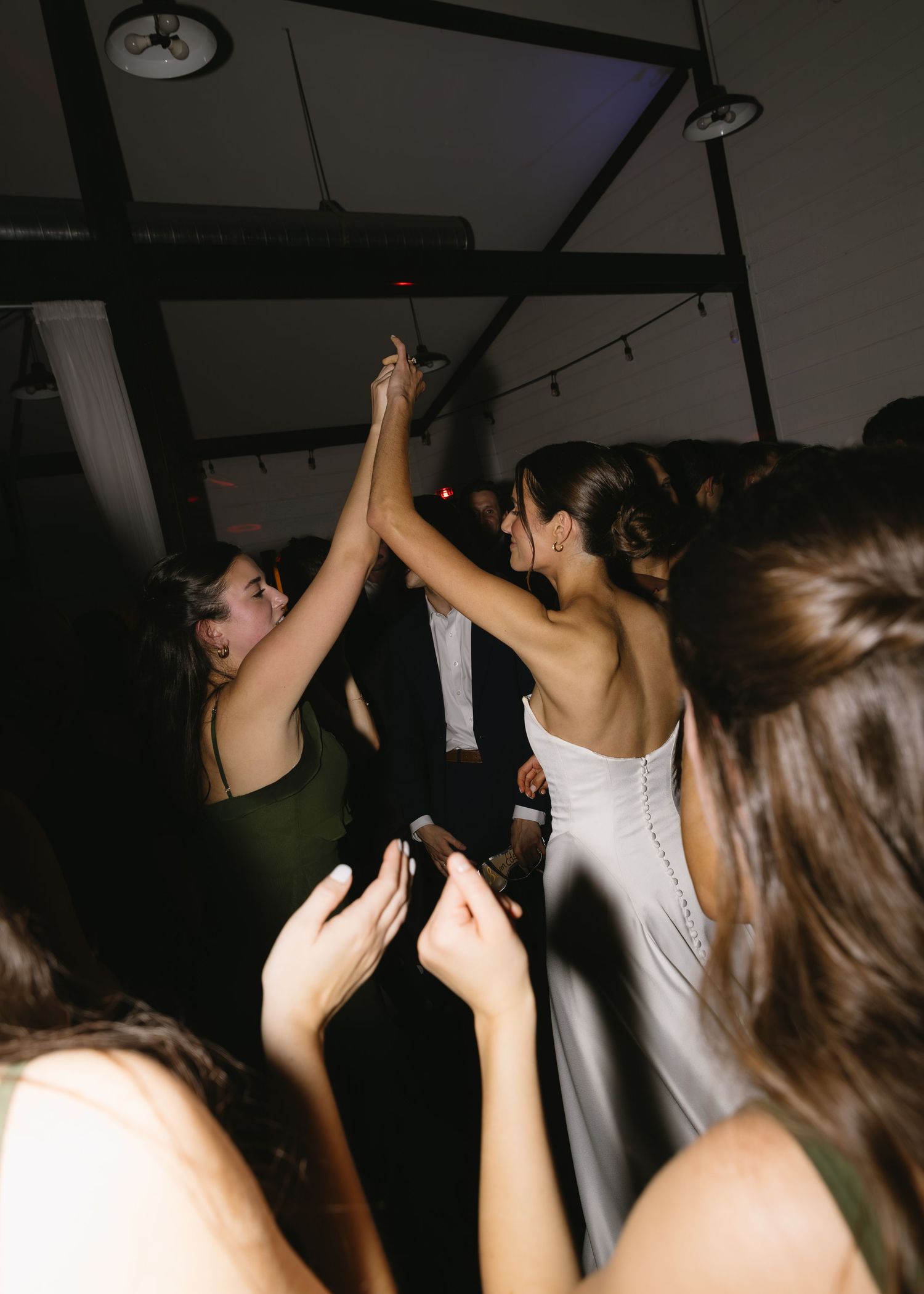 Wedding guests dance and celebrate with raised arms on a dimly lit dance floor.