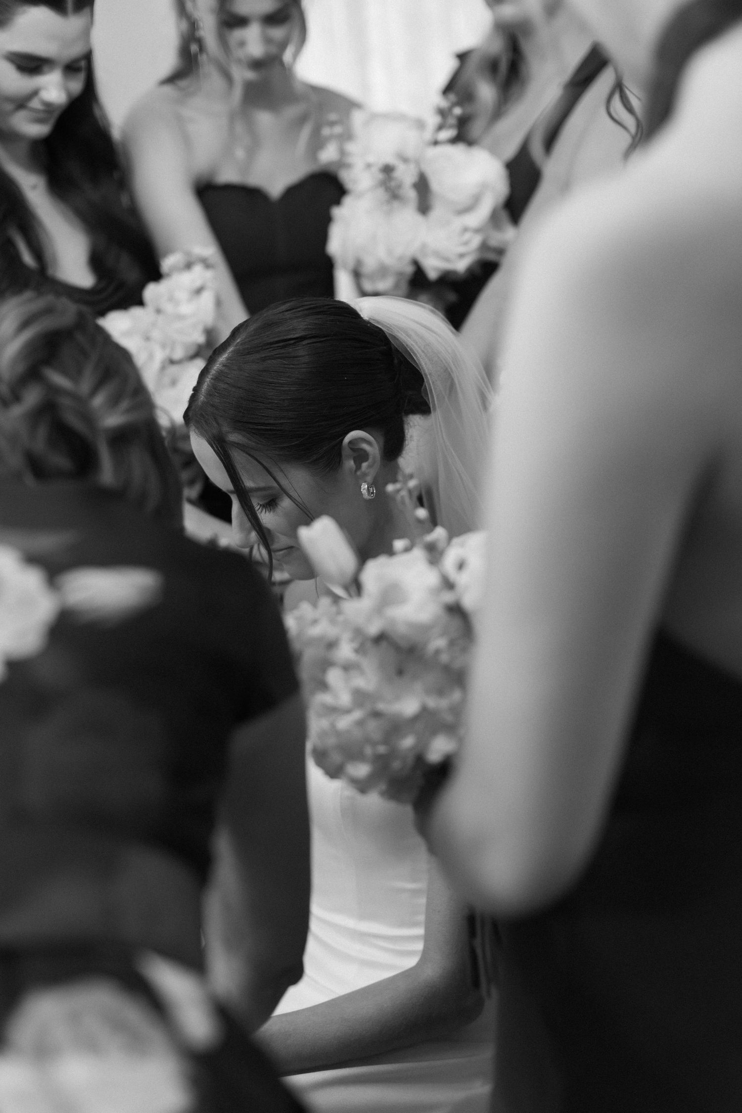 Black and white photo of wedding guests gathered around the bride holding bouquets.