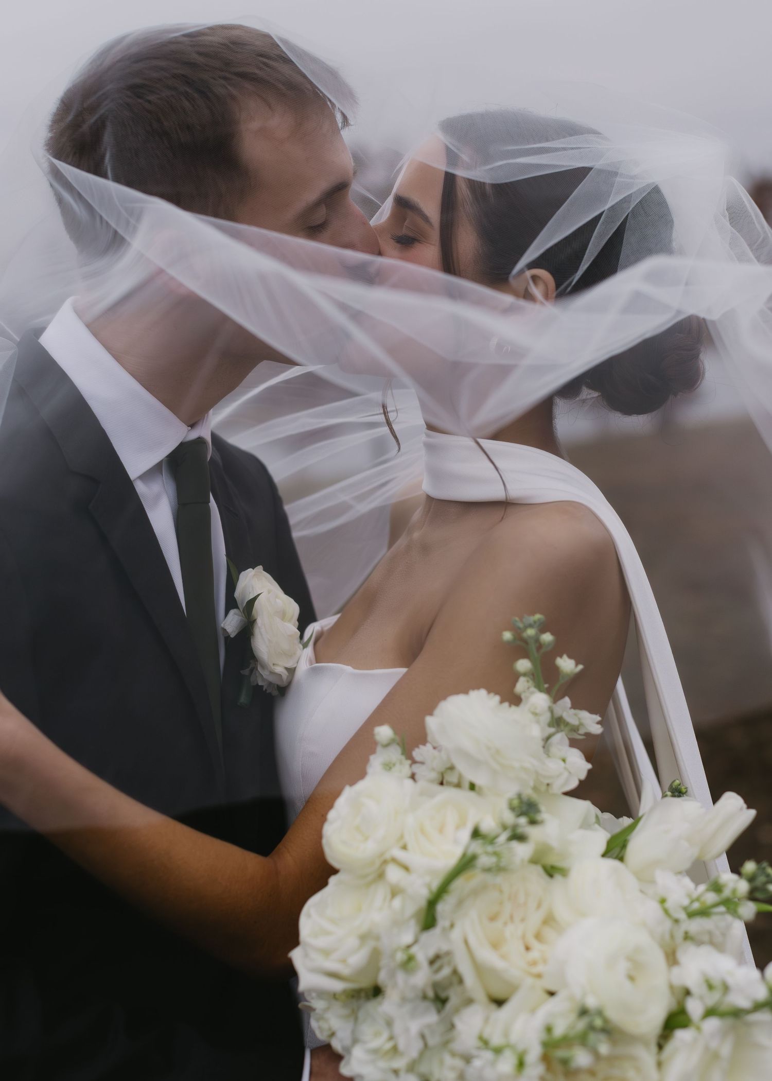 Romantic wedding moment captured with flowing veil and white rose bouquet.