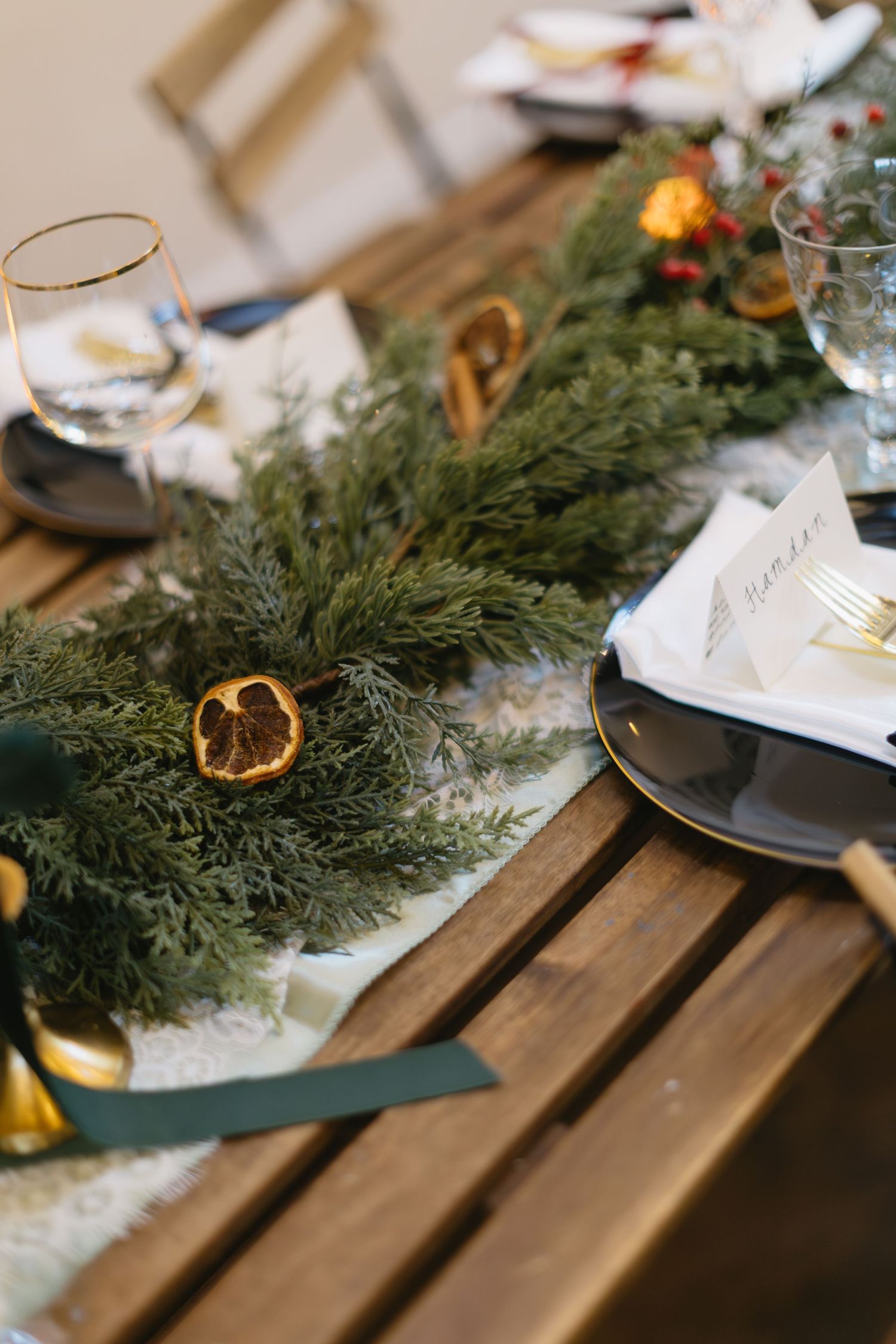 Rustic wedding table decor with evergreen garland, dried oranges, and wine glasses.
