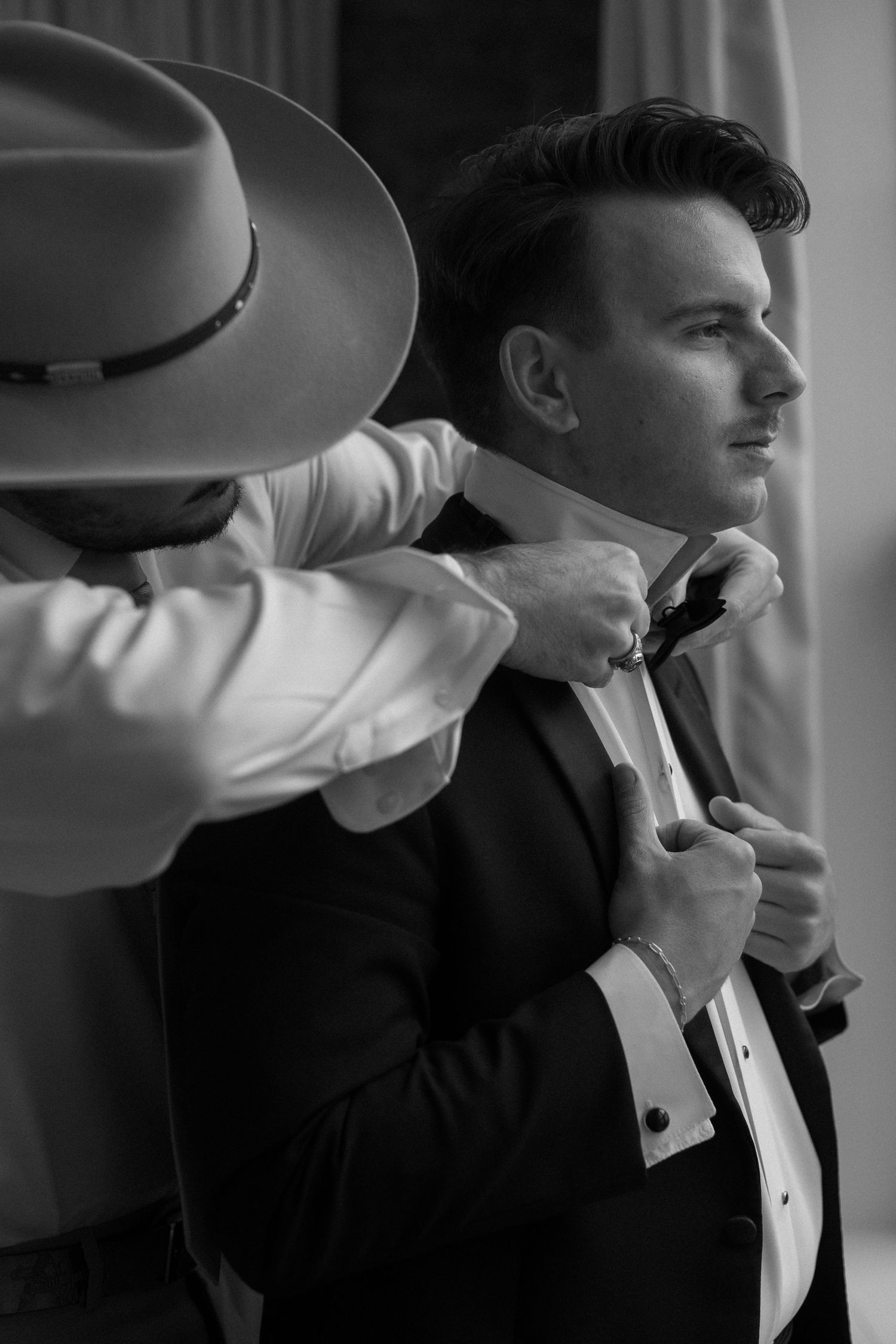 Black and white portrait series showing a groom adjusting his bow tie in a classic tuxedo.