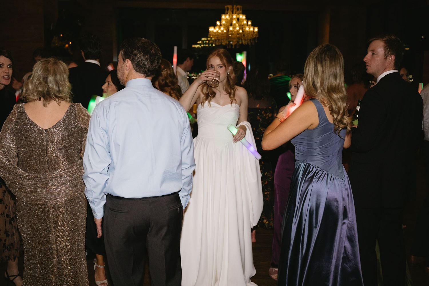 Wedding reception dance floor scene with guests in formal attire under dim lighting.