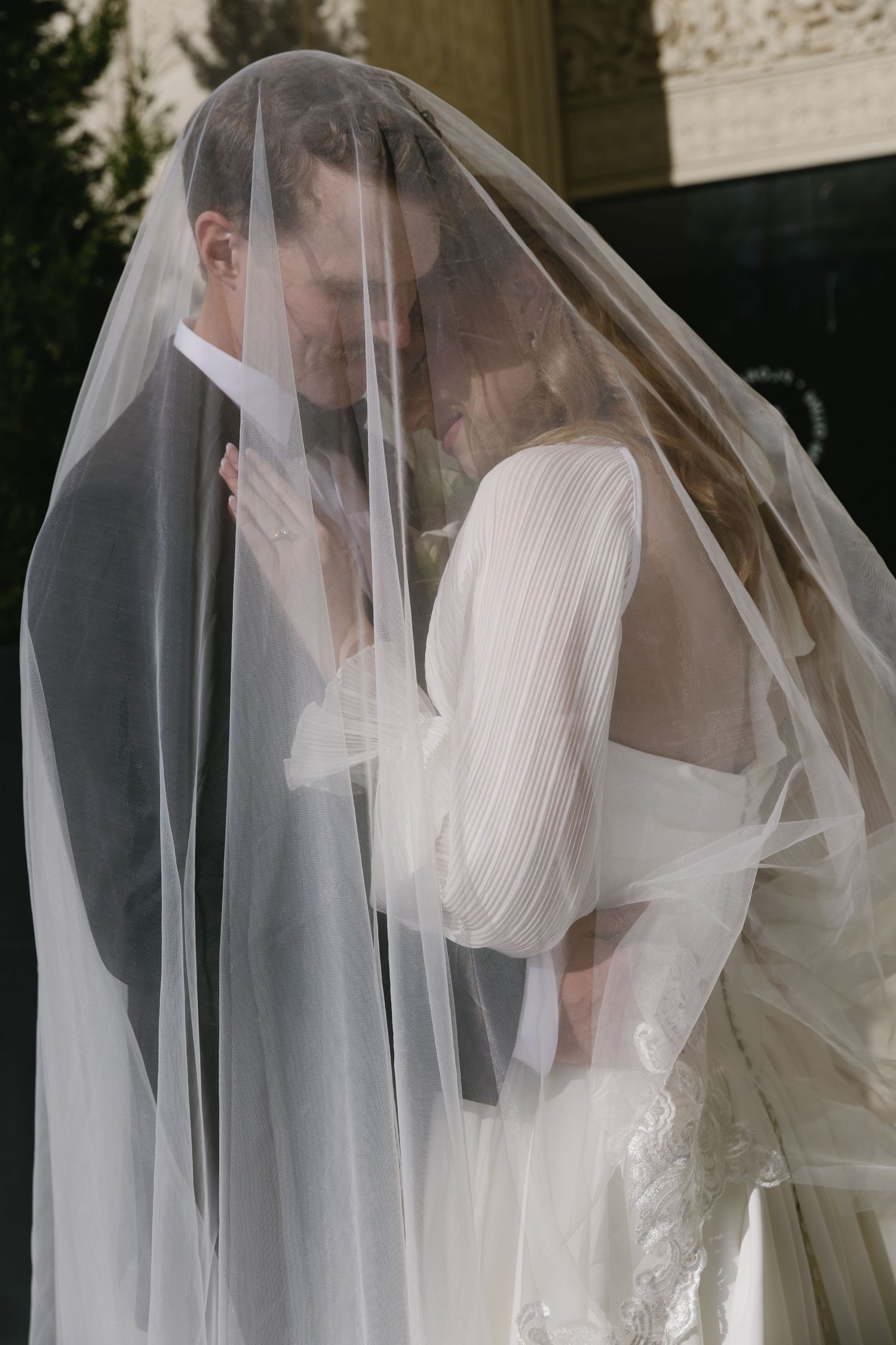 A romantic wedding moment captured through a sheer veil as a couple embraces.