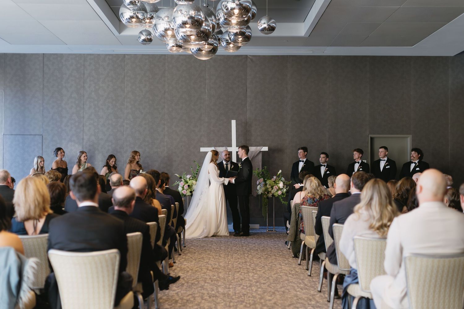 Wide shot of wedding ceremony setup with rows of white chairs in a banquet hall.