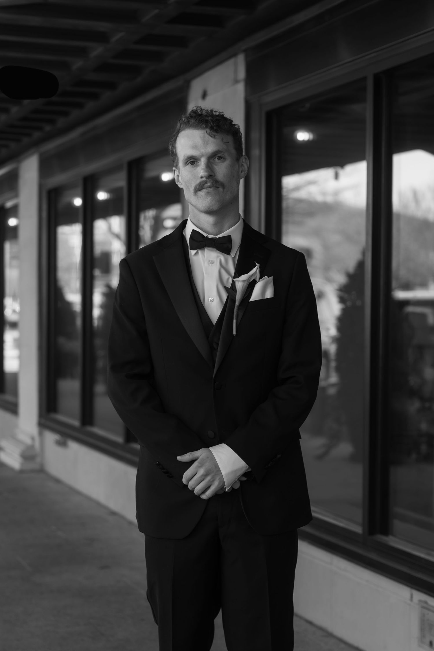 Groom in classic black tuxedo poses in moody outdoor corridor.
