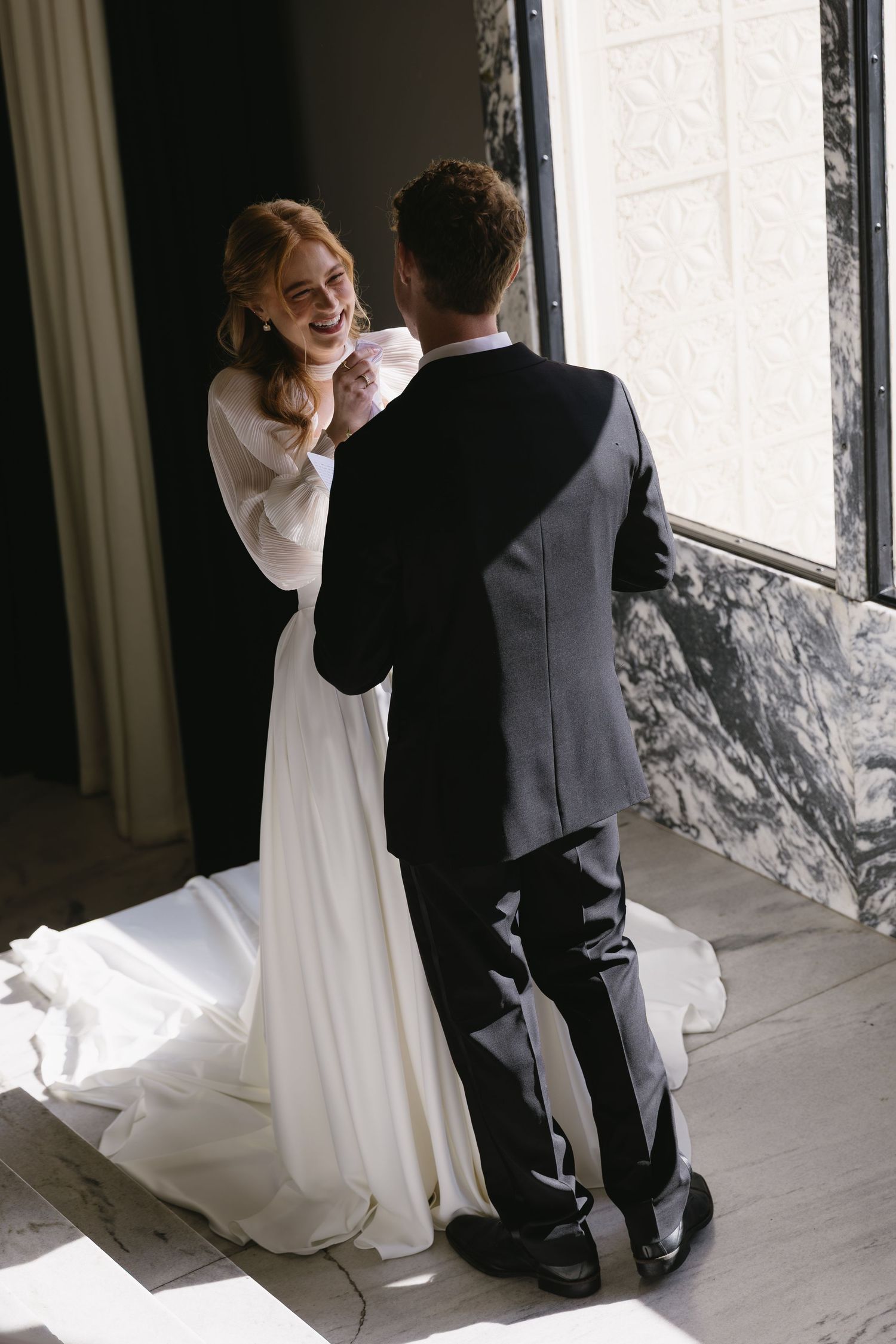 Romantic wedding moment captured against marble walls in classic black and white attire.