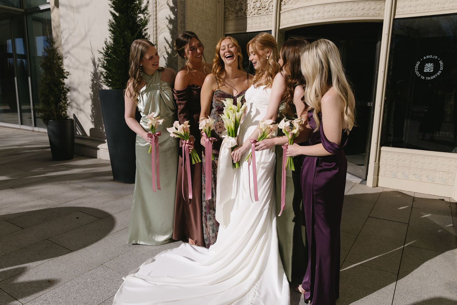 Wedding party poses outdoors with bridesmaids in purple dresses holding floral bouquets.
