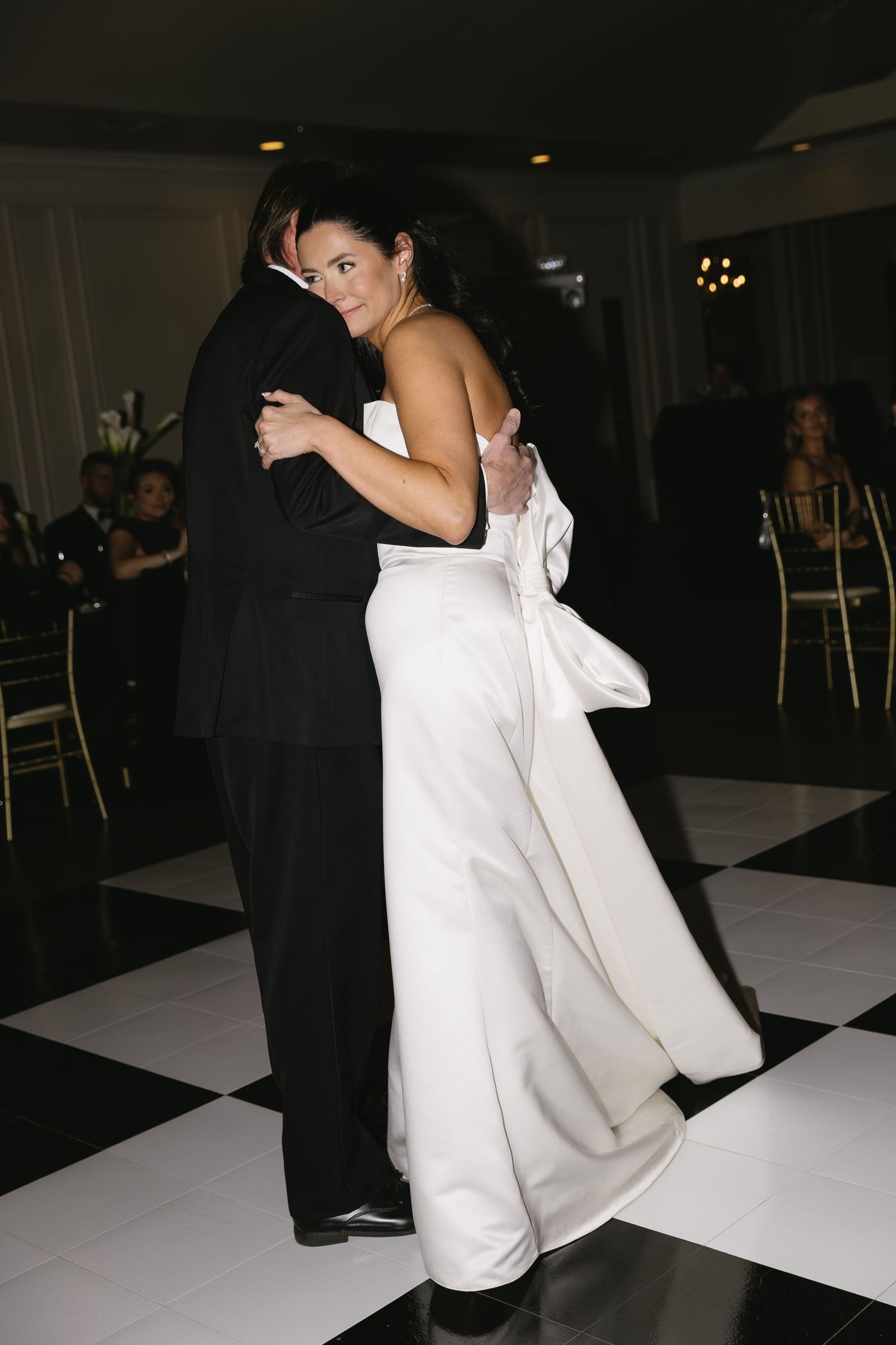 Couple dances on black and white checkered floor at wedding reception.