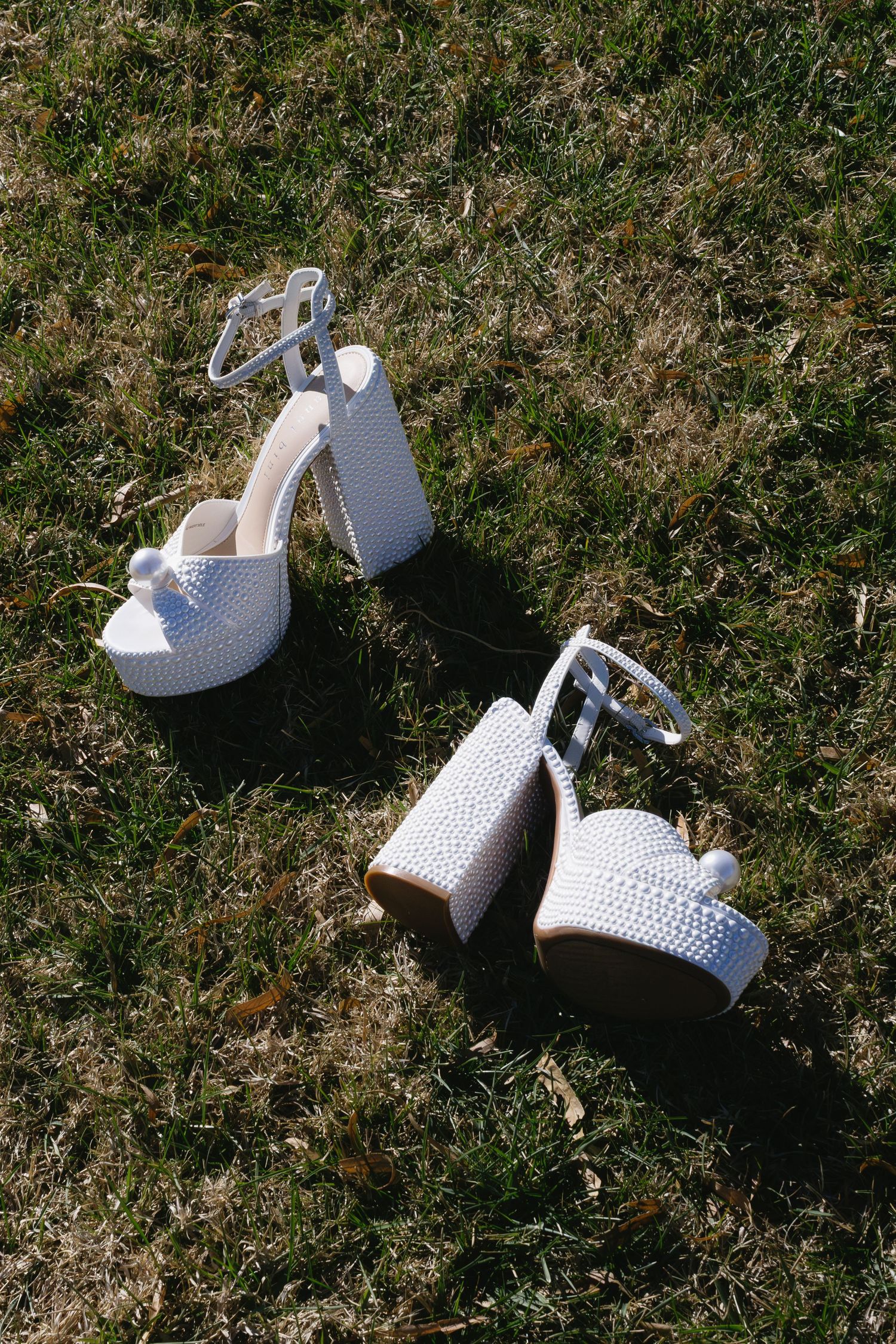 White perforated bridal shoes arranged on grass in natural lighting.
