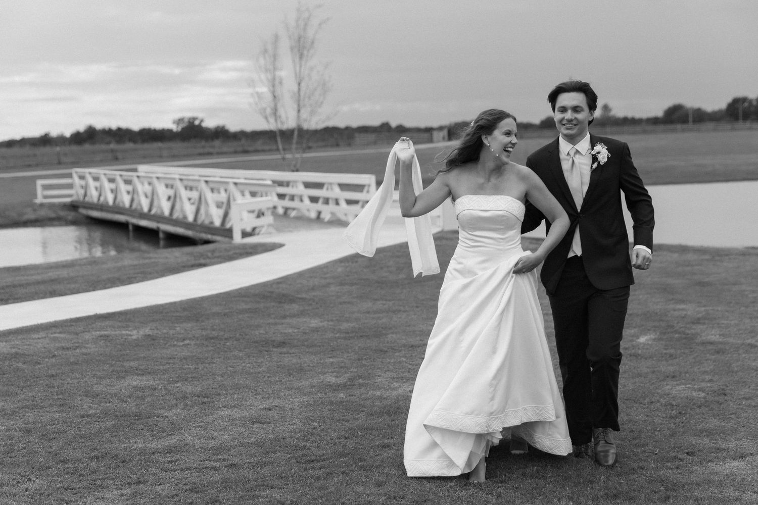 A wedding couple walks together through an outdoor garden venue past white chairs set up for a ceremony.