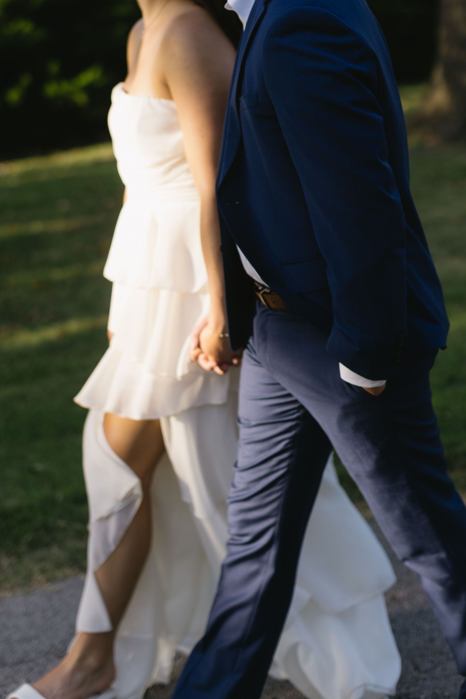Close-up of couple holding hands while walking, showing details of blue suit and flowing white dress.