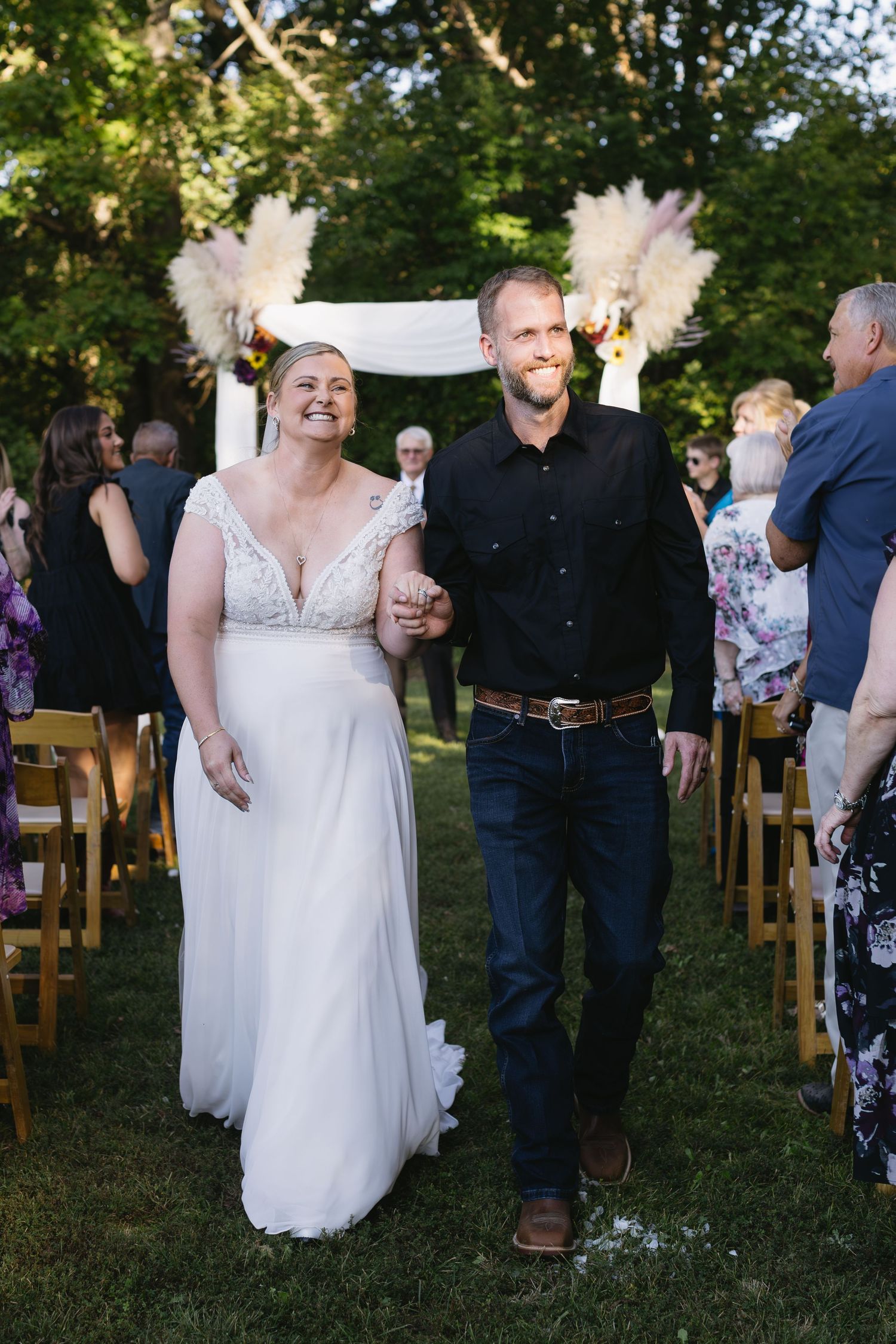 Outdoor wedding celebration with guests seated on wooden chairs under trees.