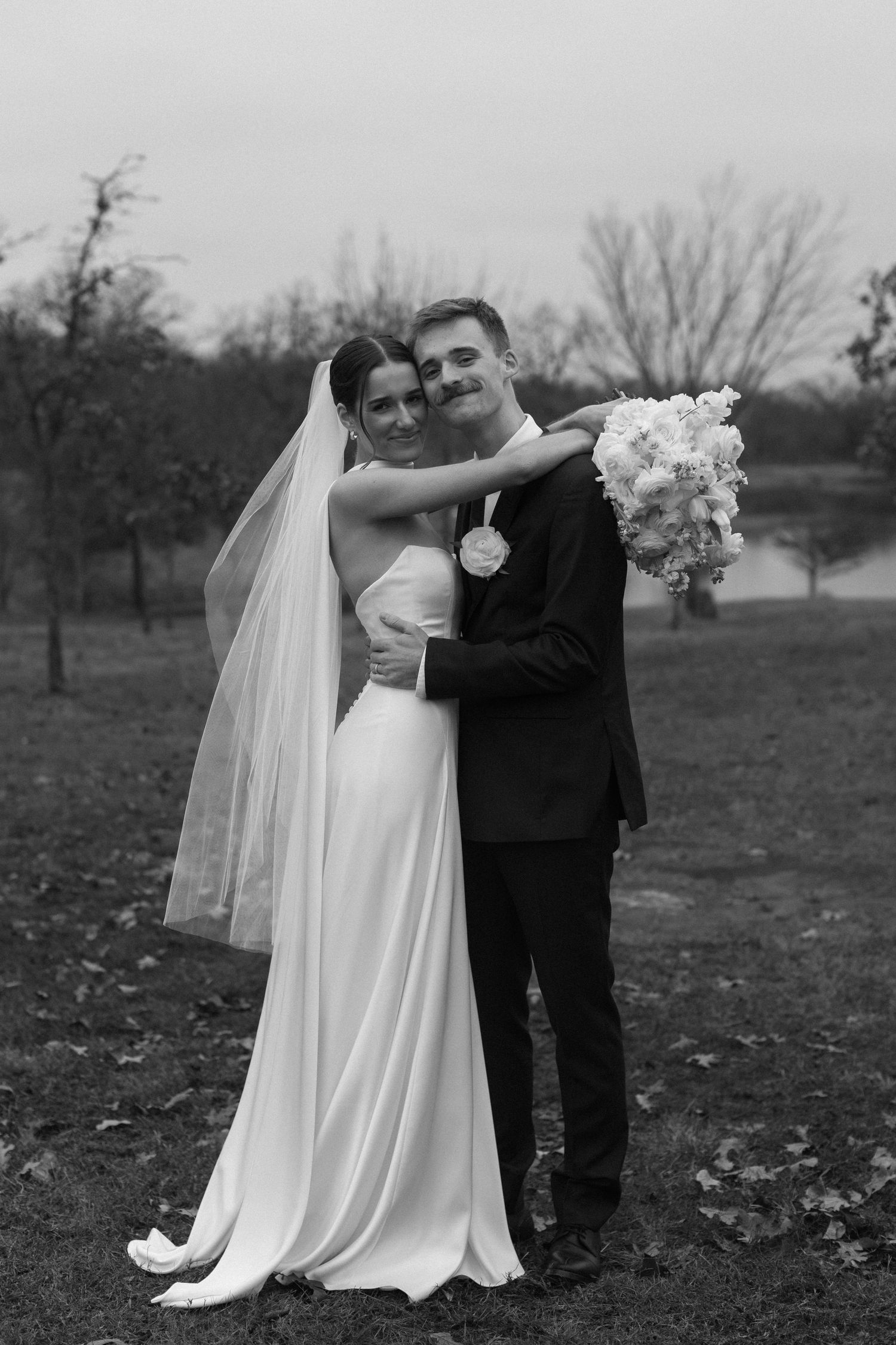A black and white wedding photo capturing a romantic moment outdoors near a lake.