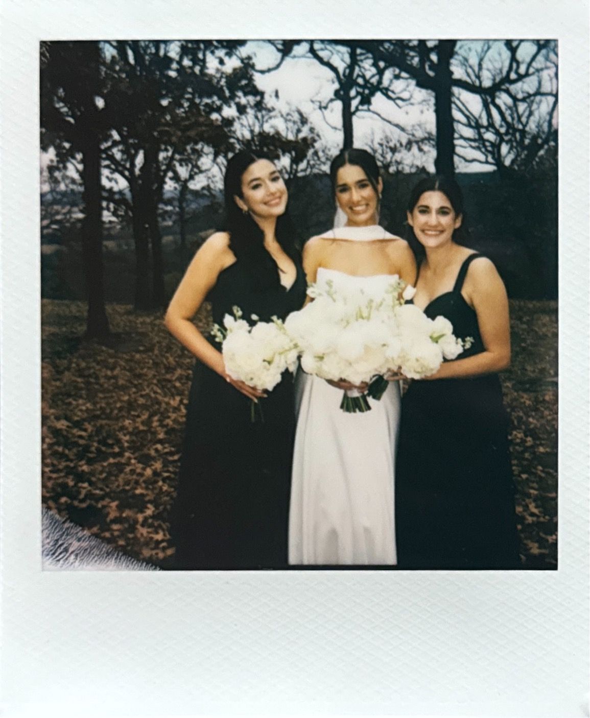 Wedding party members pose with white bouquets outdoors during an autumn celebration.