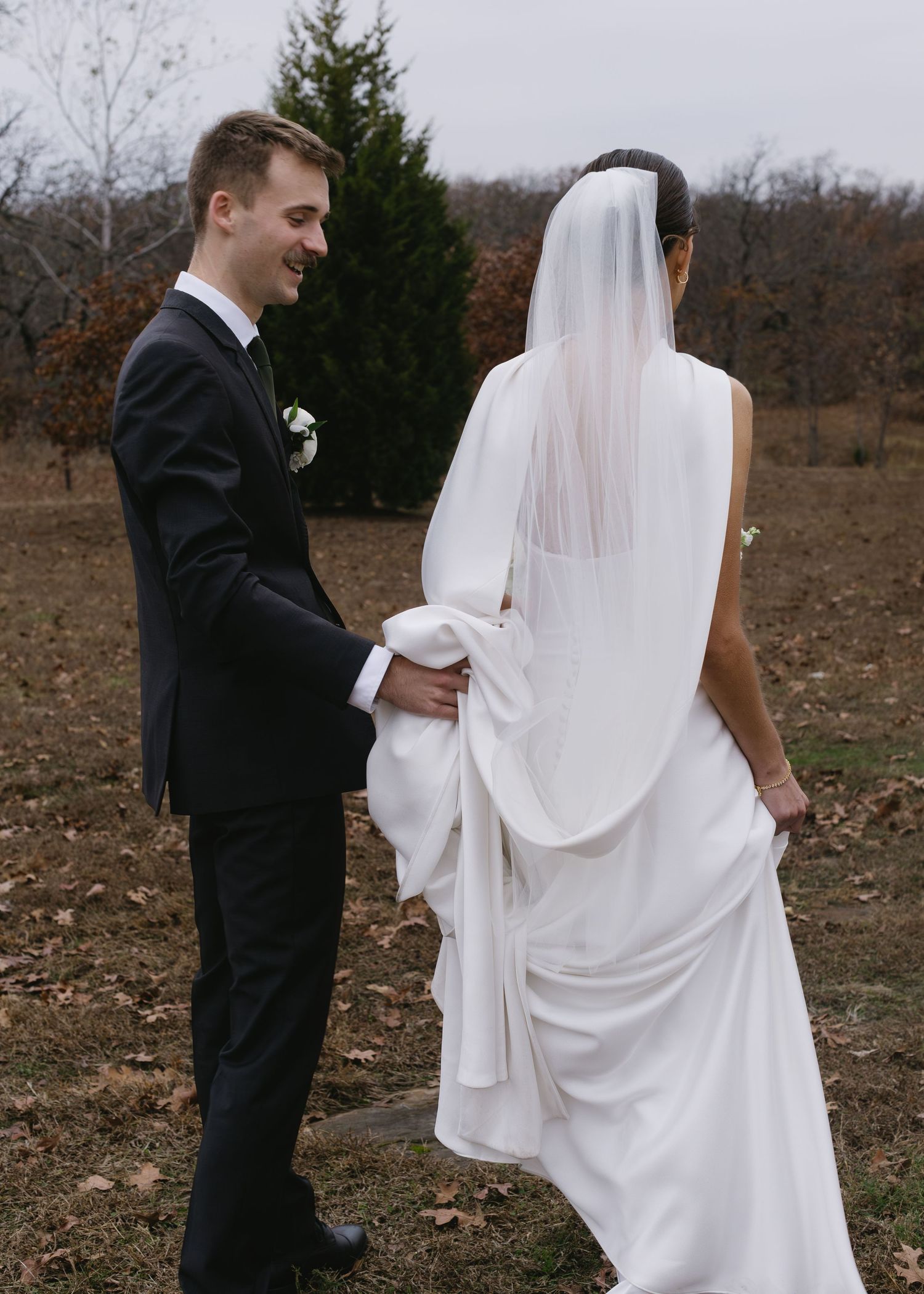 A couple in wedding attire walks together across a fall landscape.