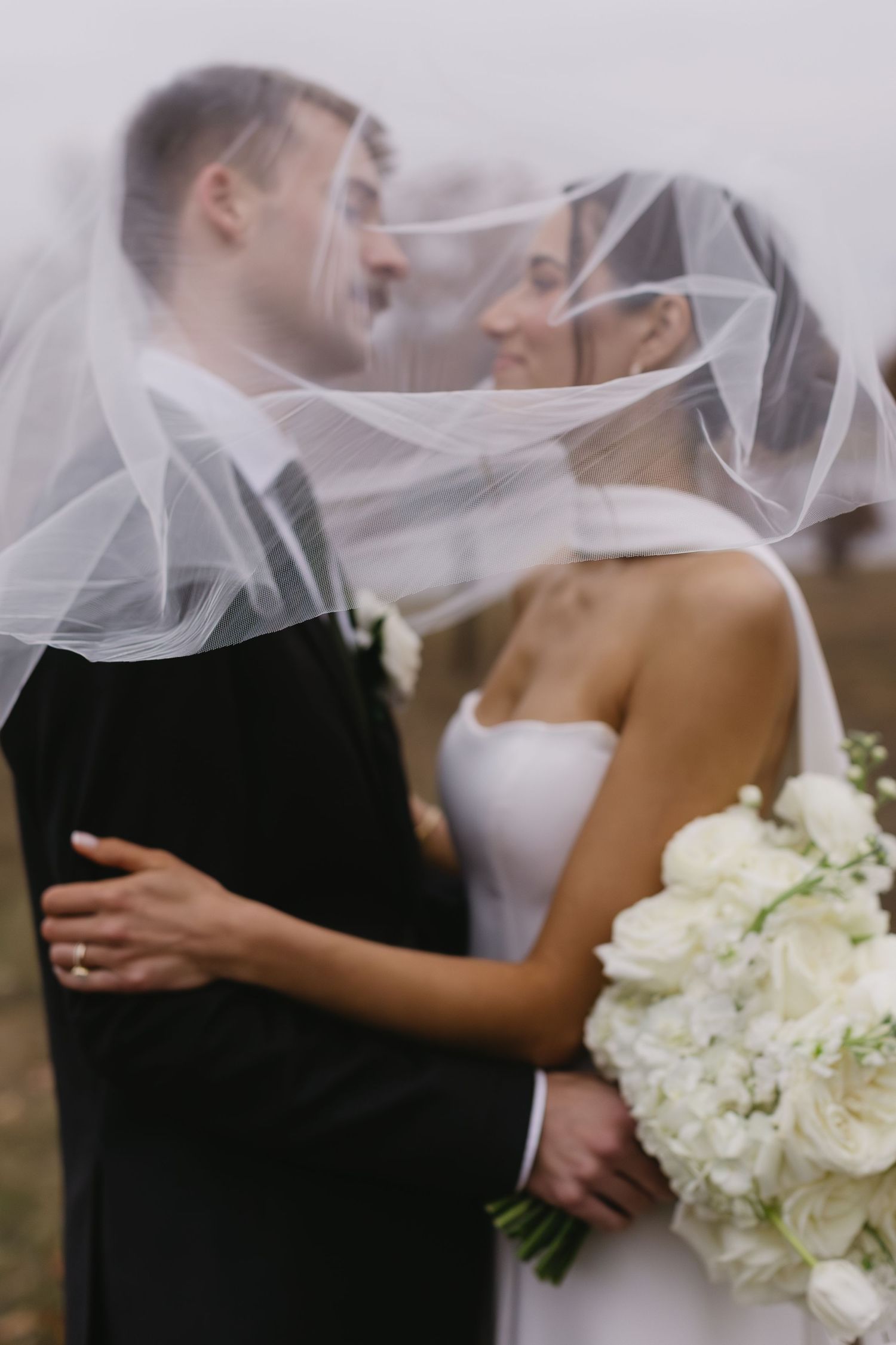 Romantic wedding portrait through delicate veil with white floral bouquet.