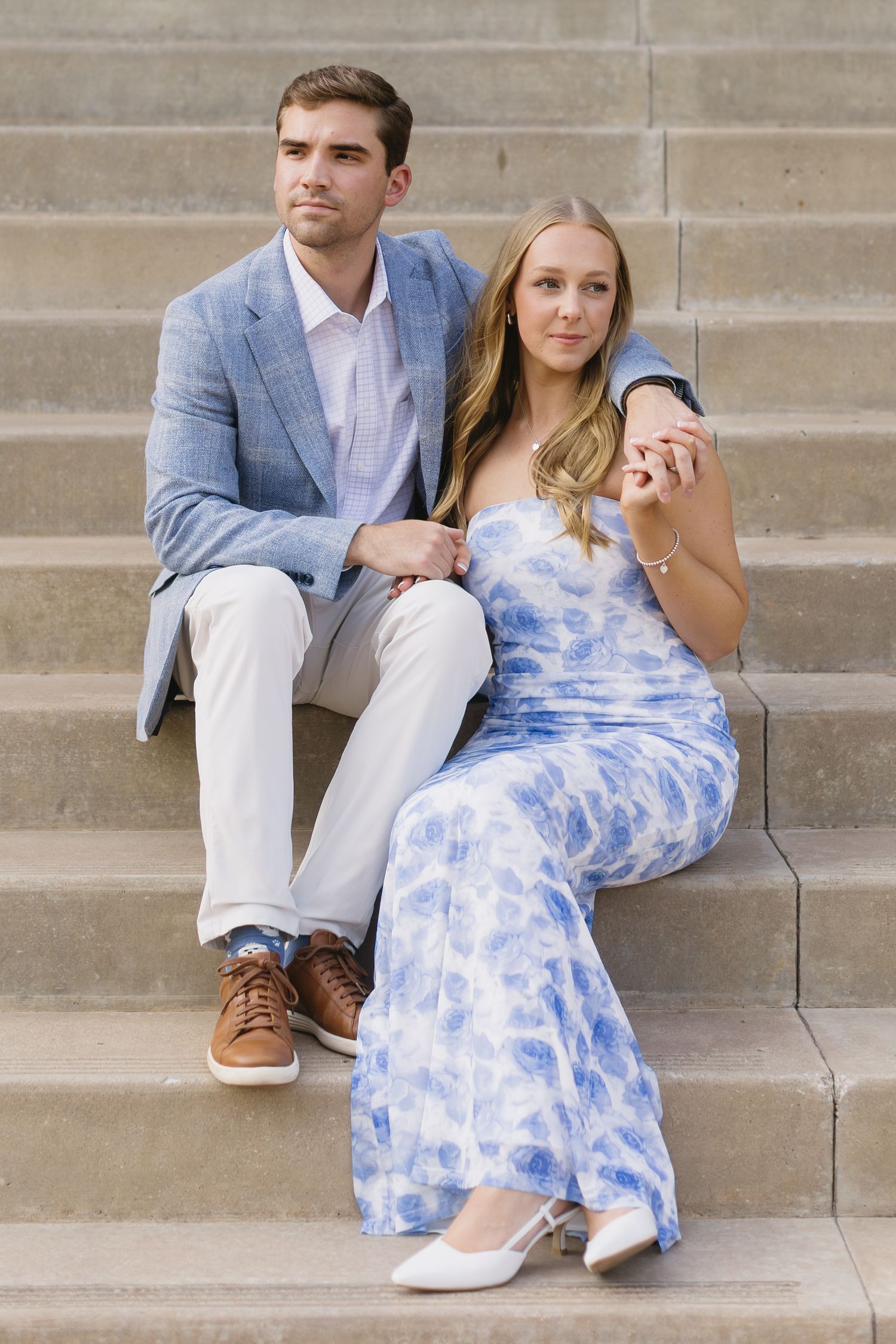 A couple in coordinated blue and white outfits sits together on concrete steps during a photo session.