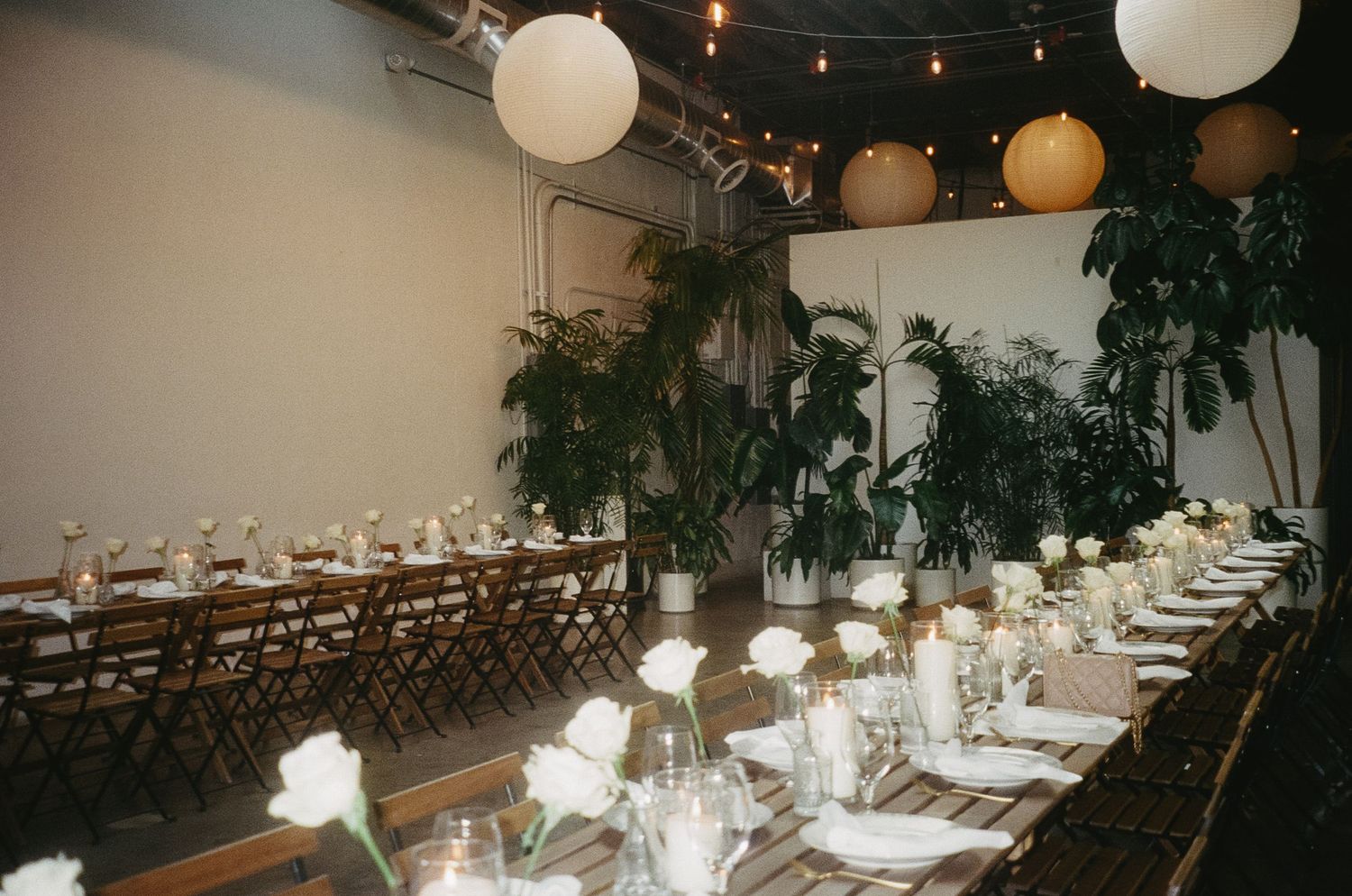 Elegant wedding reception venue with long tables, white lanterns, and greenery decorations.