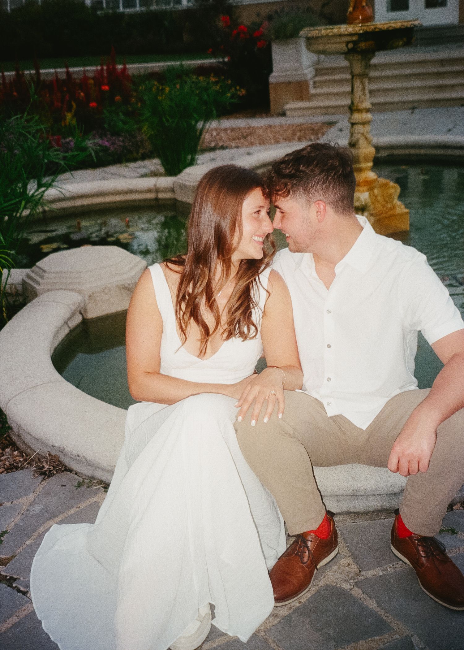 A couple in white attire share intimate moments while seated on stone steps in a romantic outdoor setting.