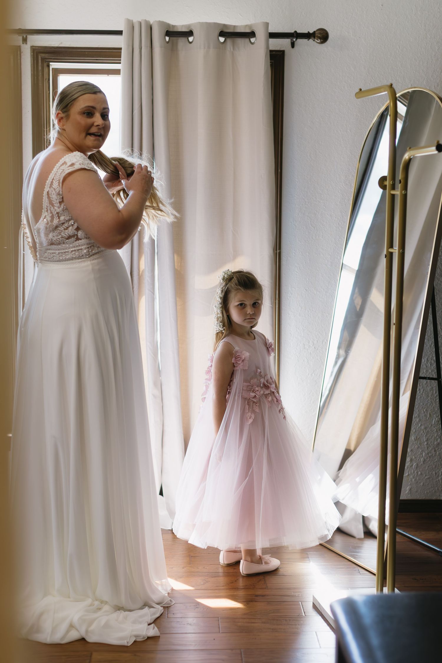 A touching getting-ready moment with two figures in white dresses standing by a full-length mirror.