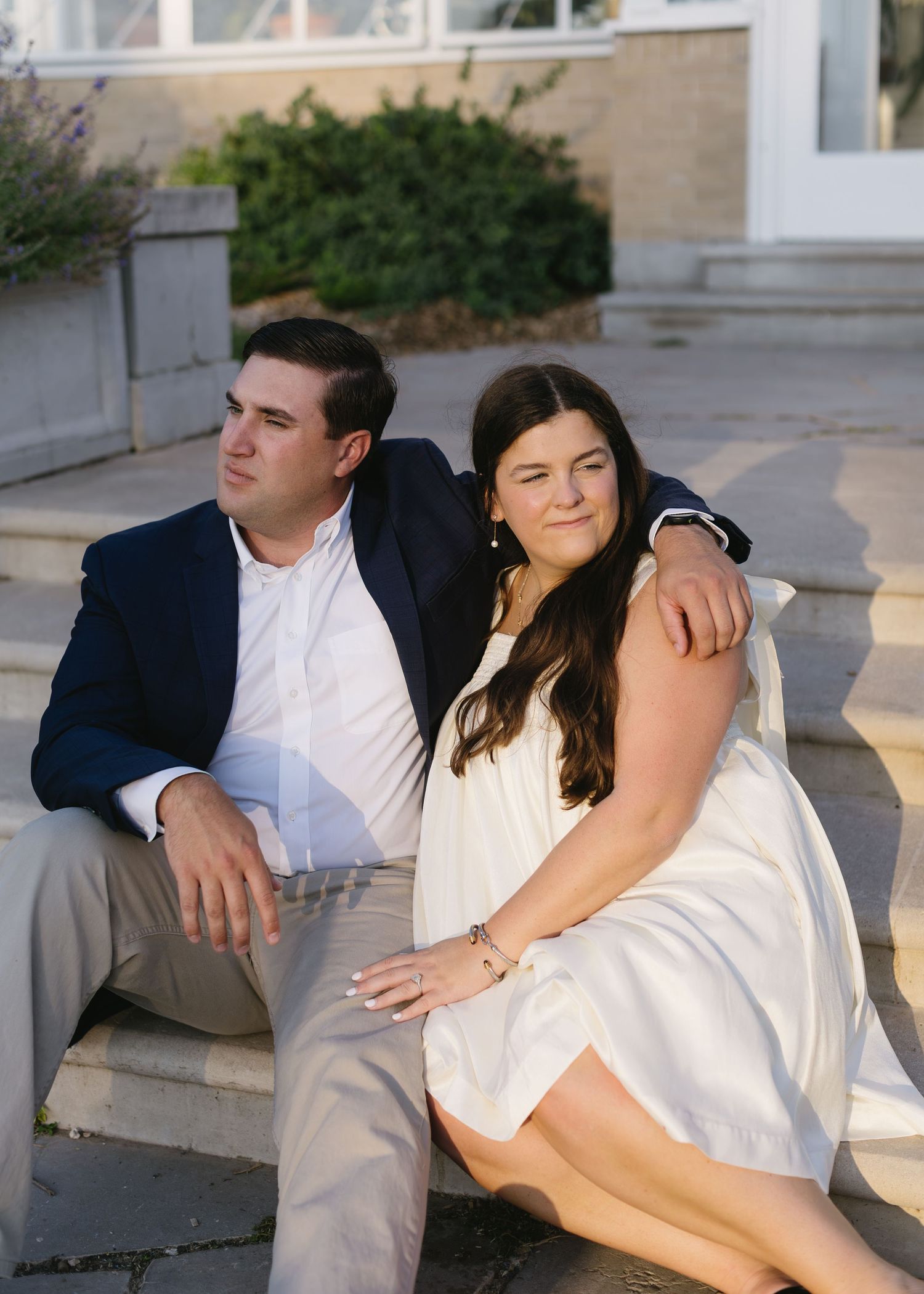 A couple relaxes and poses together on white porch steps in formal attire.