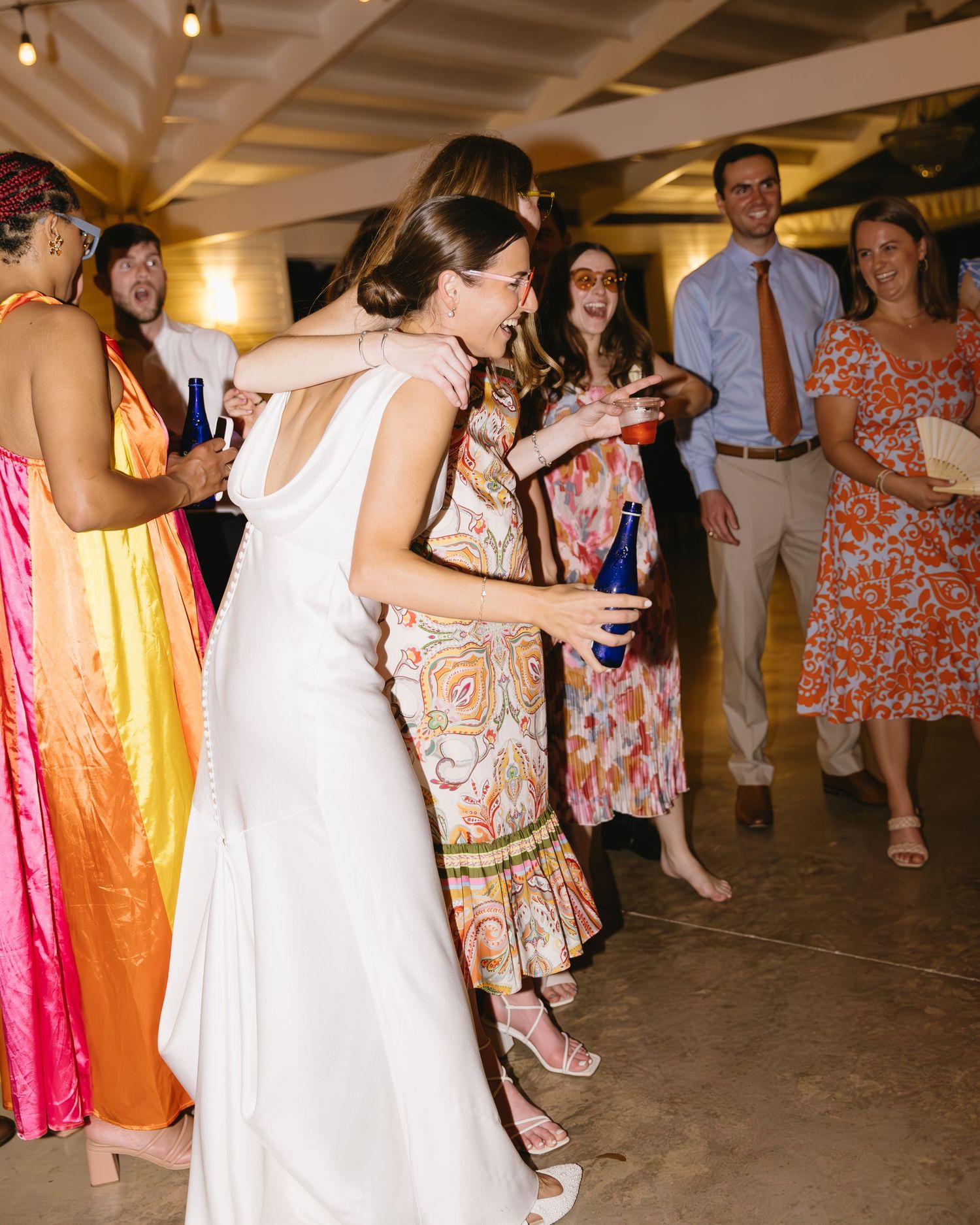 Wedding reception celebration with guests dancing in colorful dresses and formal attire.