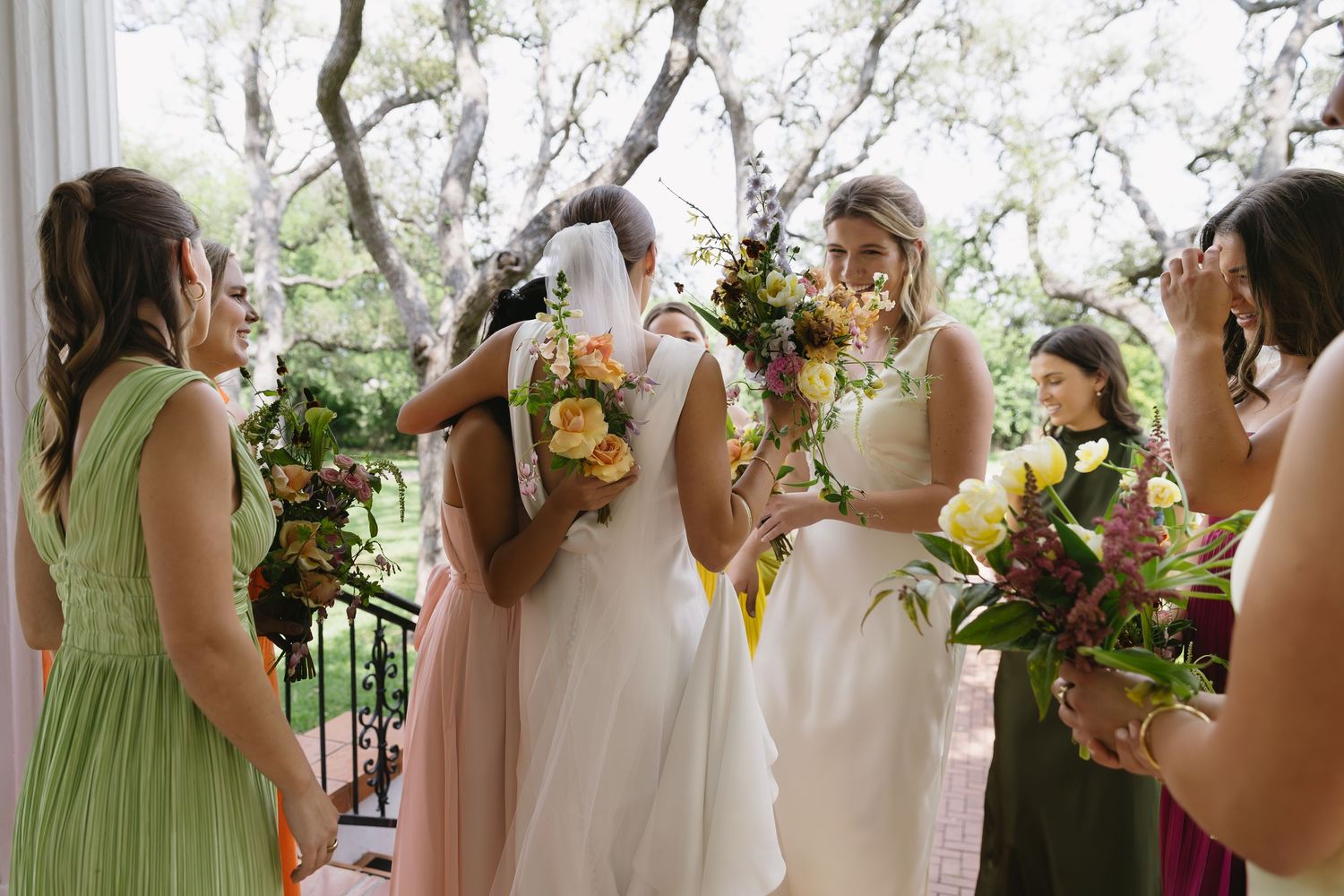 Row of bridesmaids in mint green and blush dresses holding floral bouquets at an outdoor wedding ceremony.