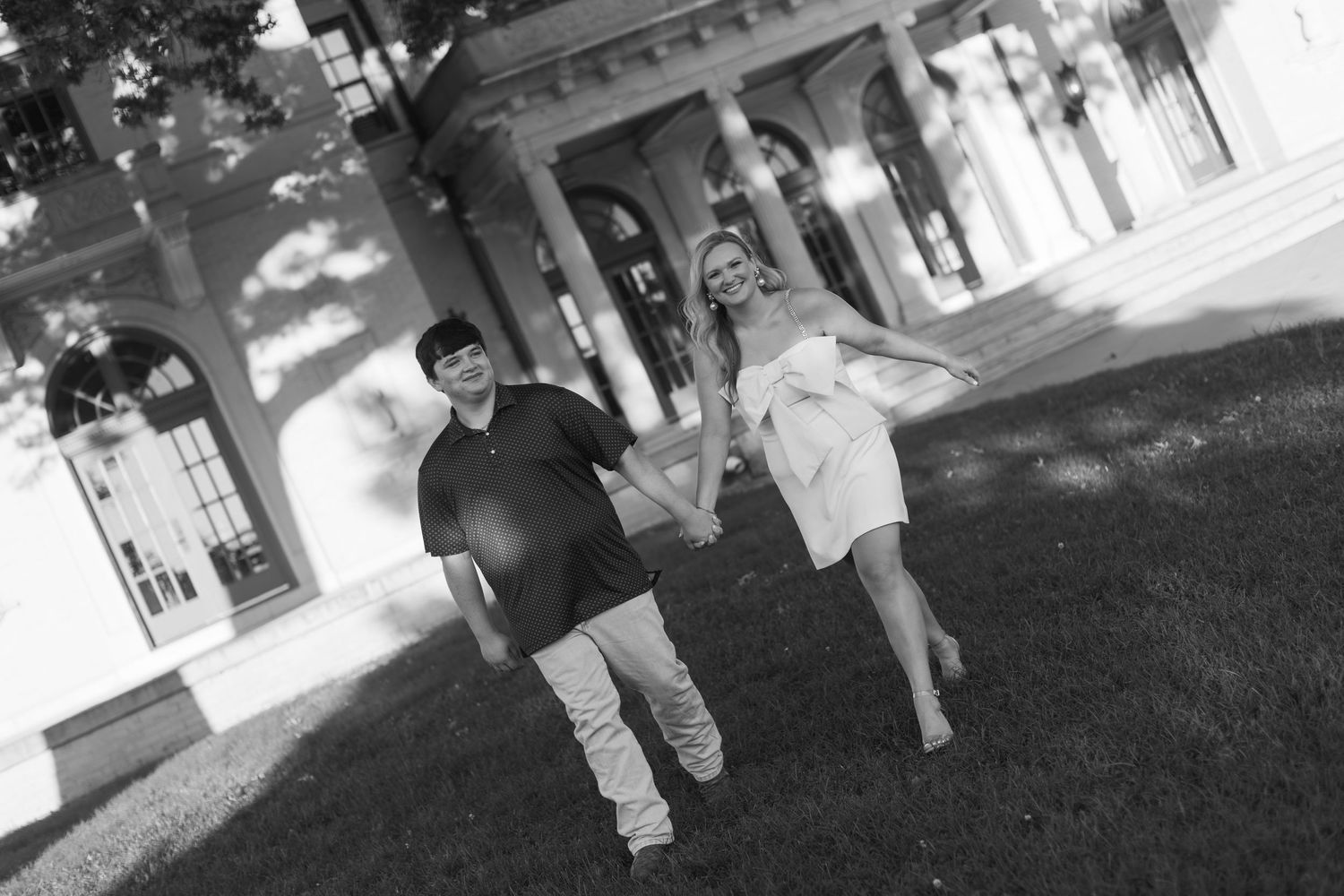 Black and white photo of two people walking together outdoors in front of a building with columns on a sunny day.