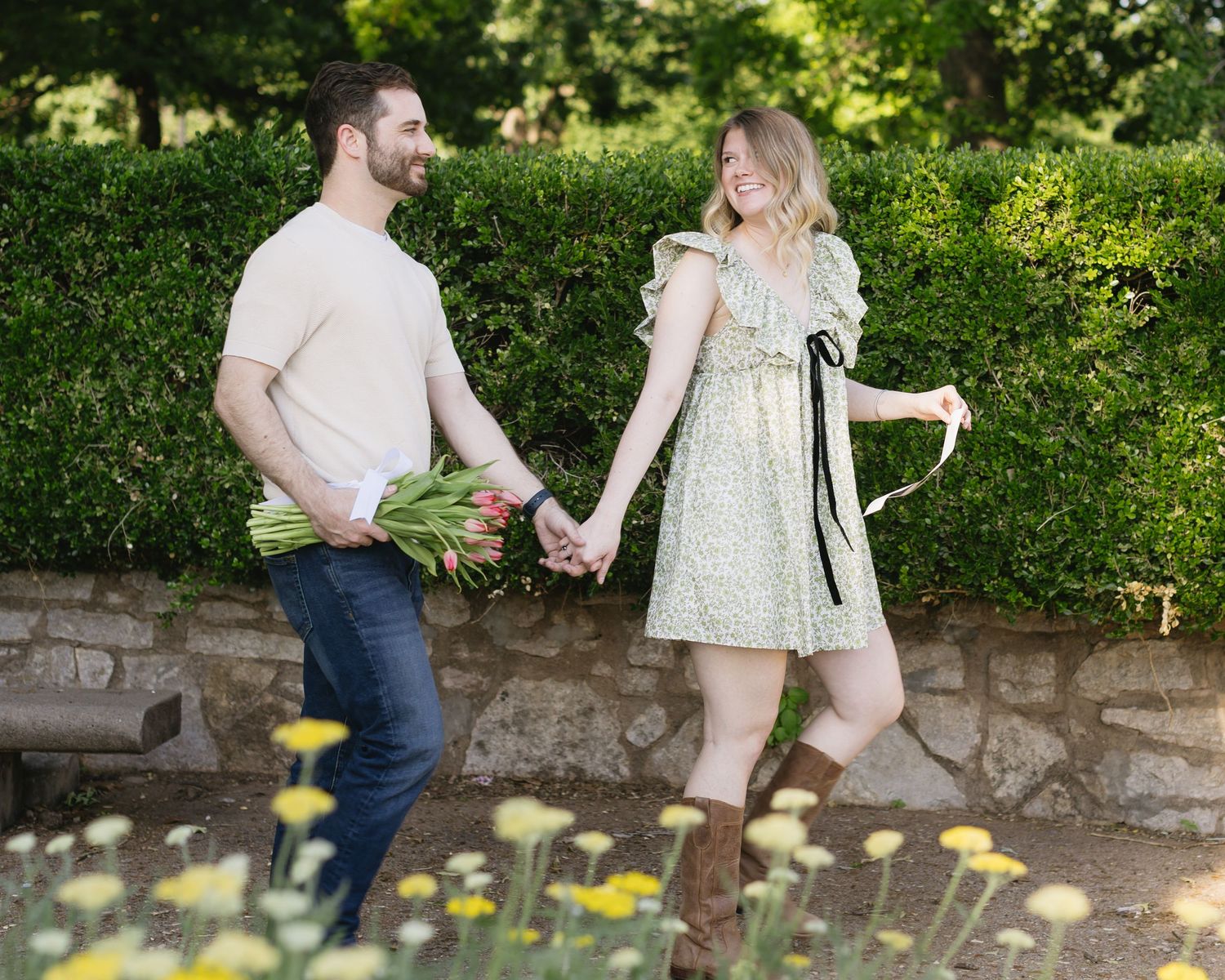 A couple walks along a garden path with yellow flowers in the foreground, creating a romantic outdoor scene.