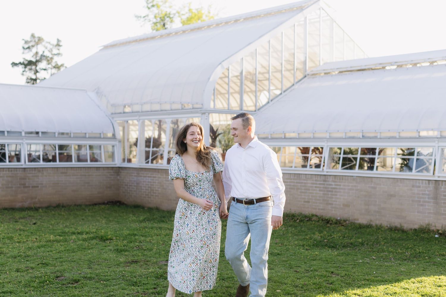 A couple poses together in front of a white building on a sunny spring day.